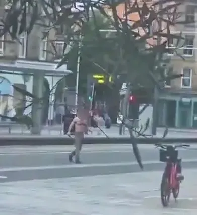 A shirtless person in shorts walks on a paved street.