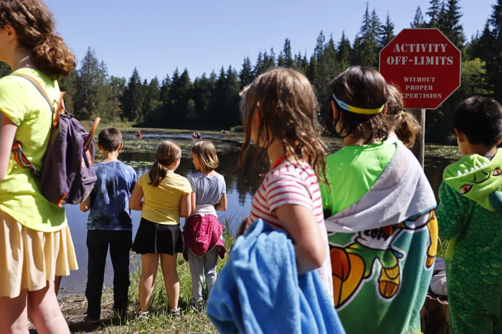 Campers at a Jewish summer camp look out at a lake with several people in canoes, with a red 