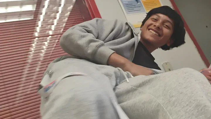 Young man in a gray hoodie and sweatpants smiling.