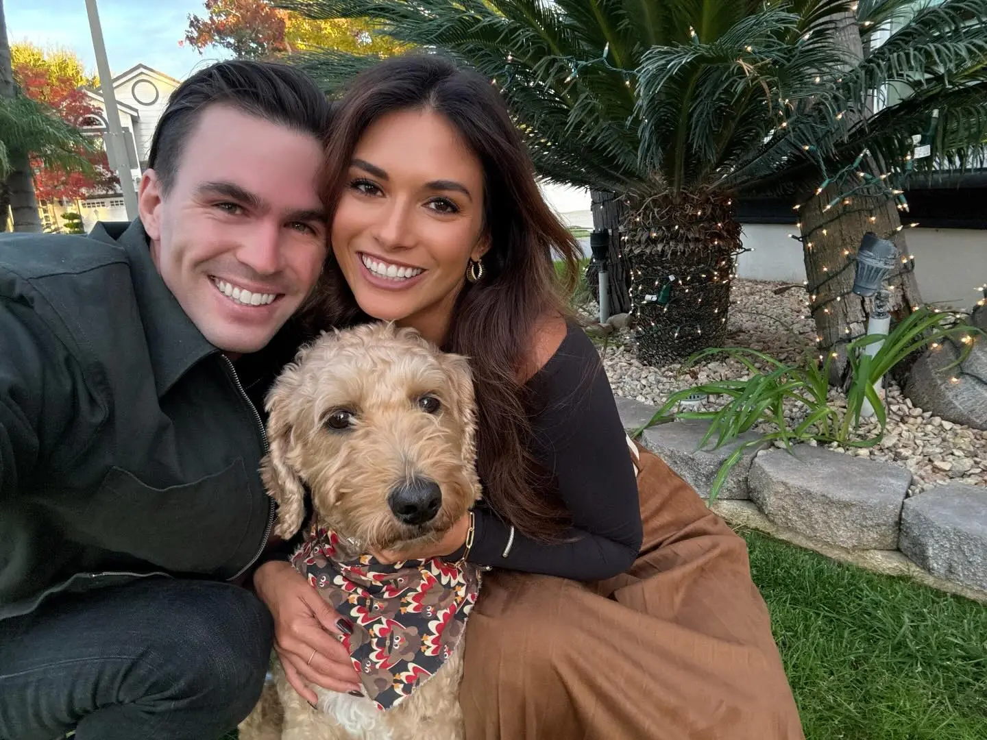 A couple and their goldendoodle posing outdoors.