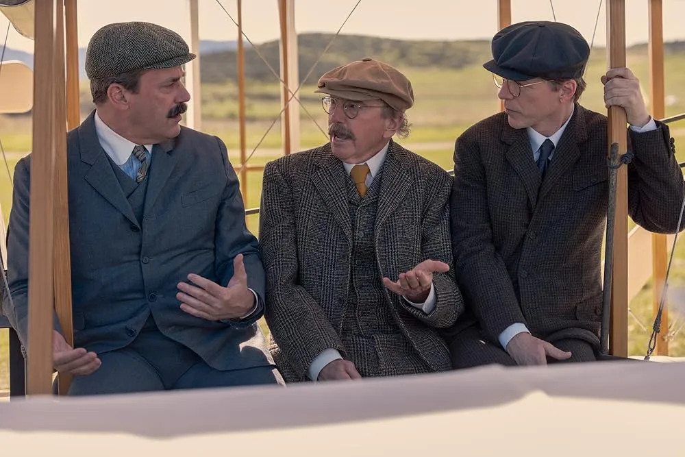 Three men in historical clothing sit in a plane and converse.