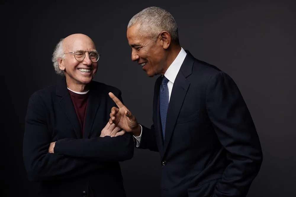 Larry David laughing while Barack Obama points and smiles.