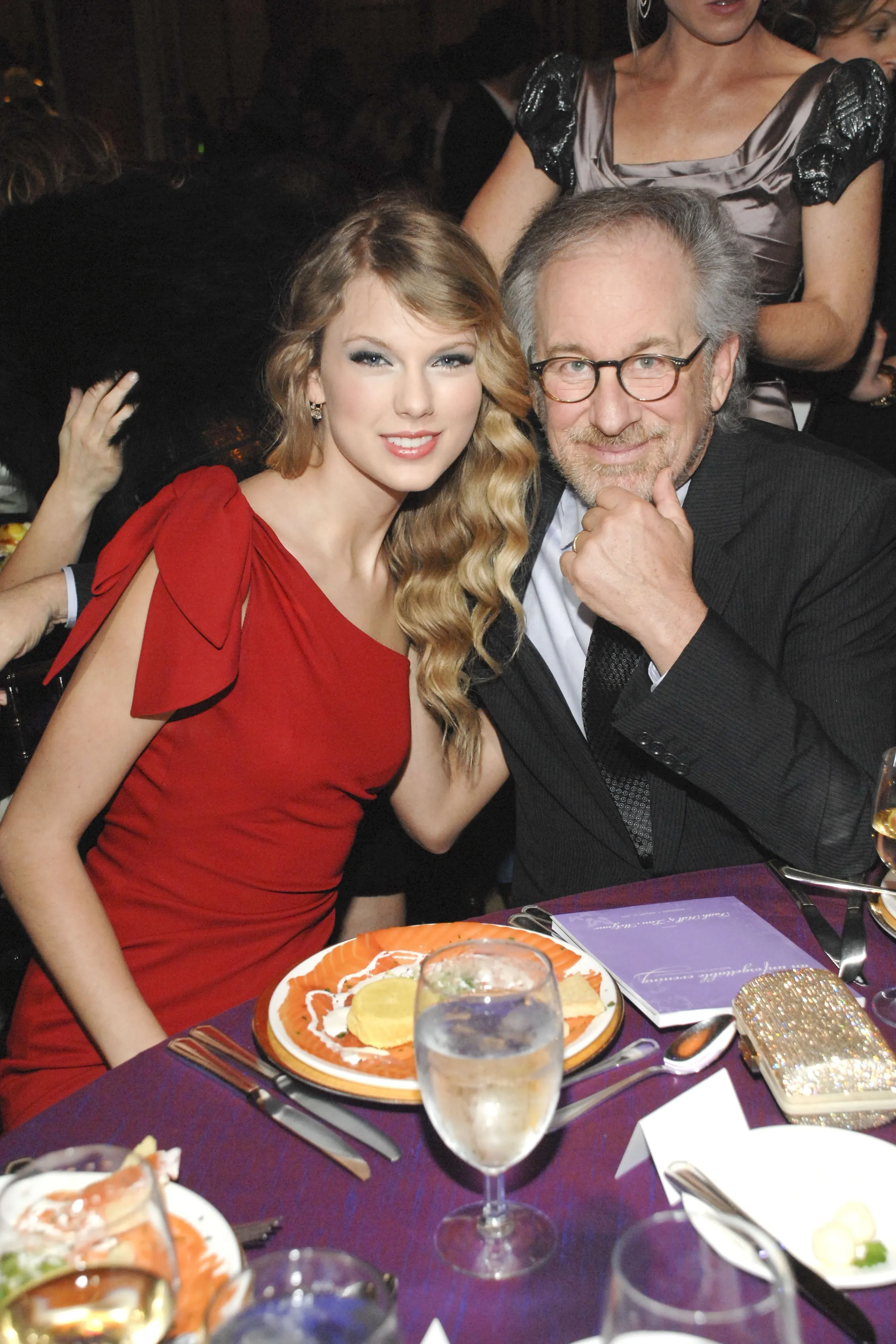 Taylor Swift and Steven Spielberg sitting at a table.