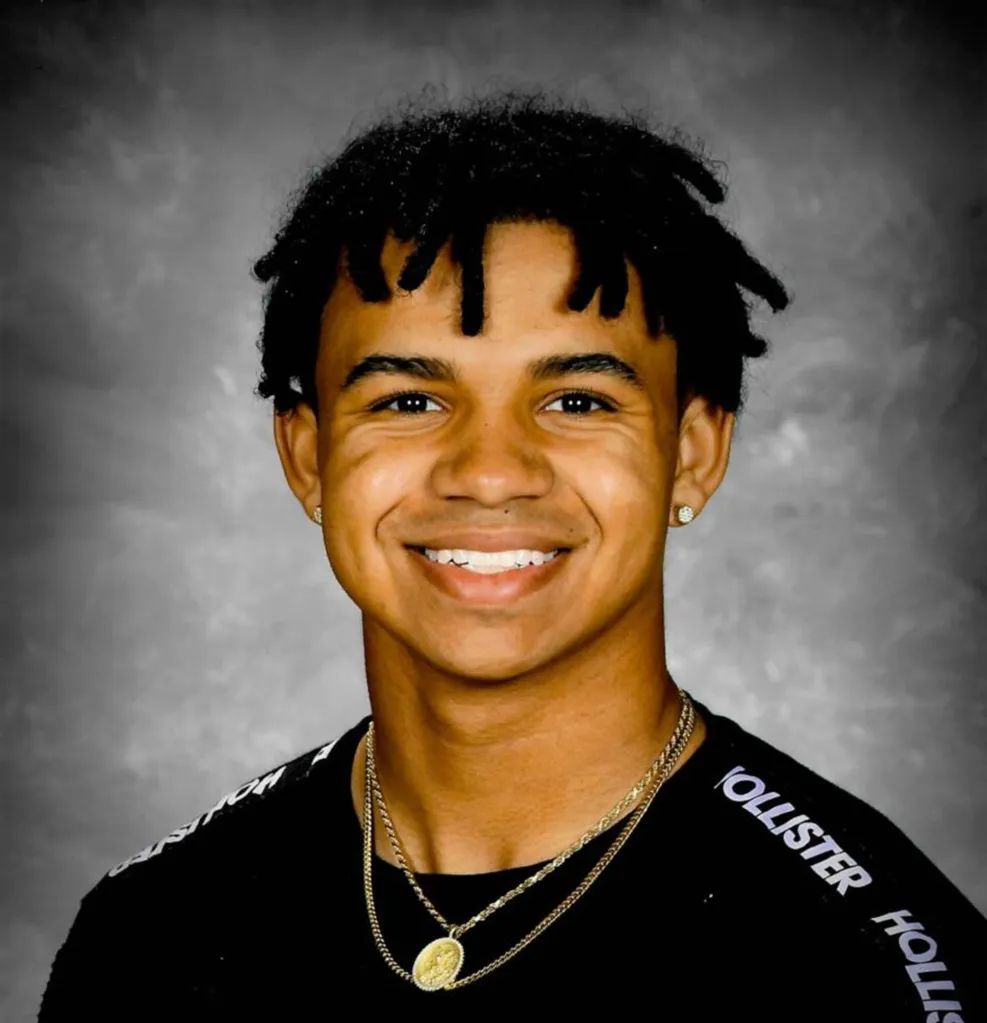 Davion Flanagan, a young man with dark curly hair and a gold chain, smiling at the camera.