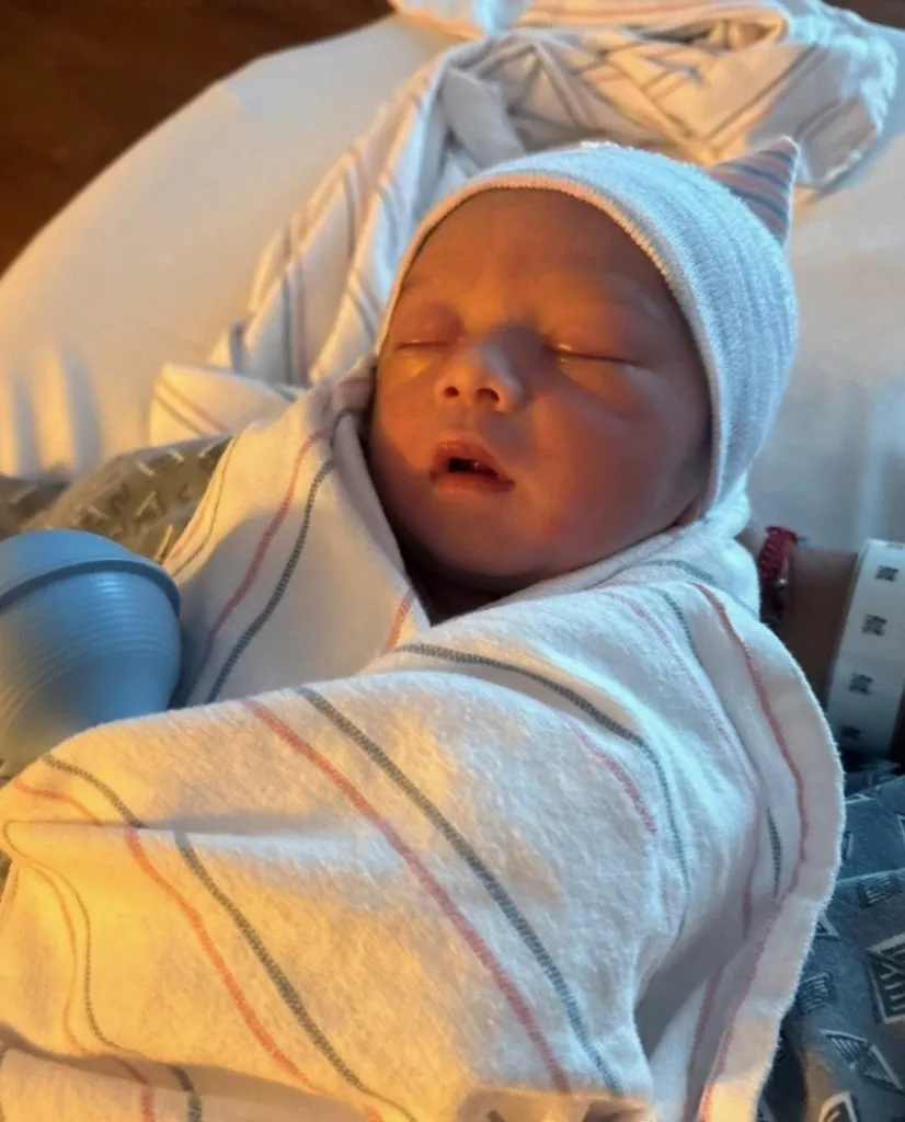 Newborn baby Mateo Gonzalez sleeping, swaddled in a blanket and wearing a striped hat.