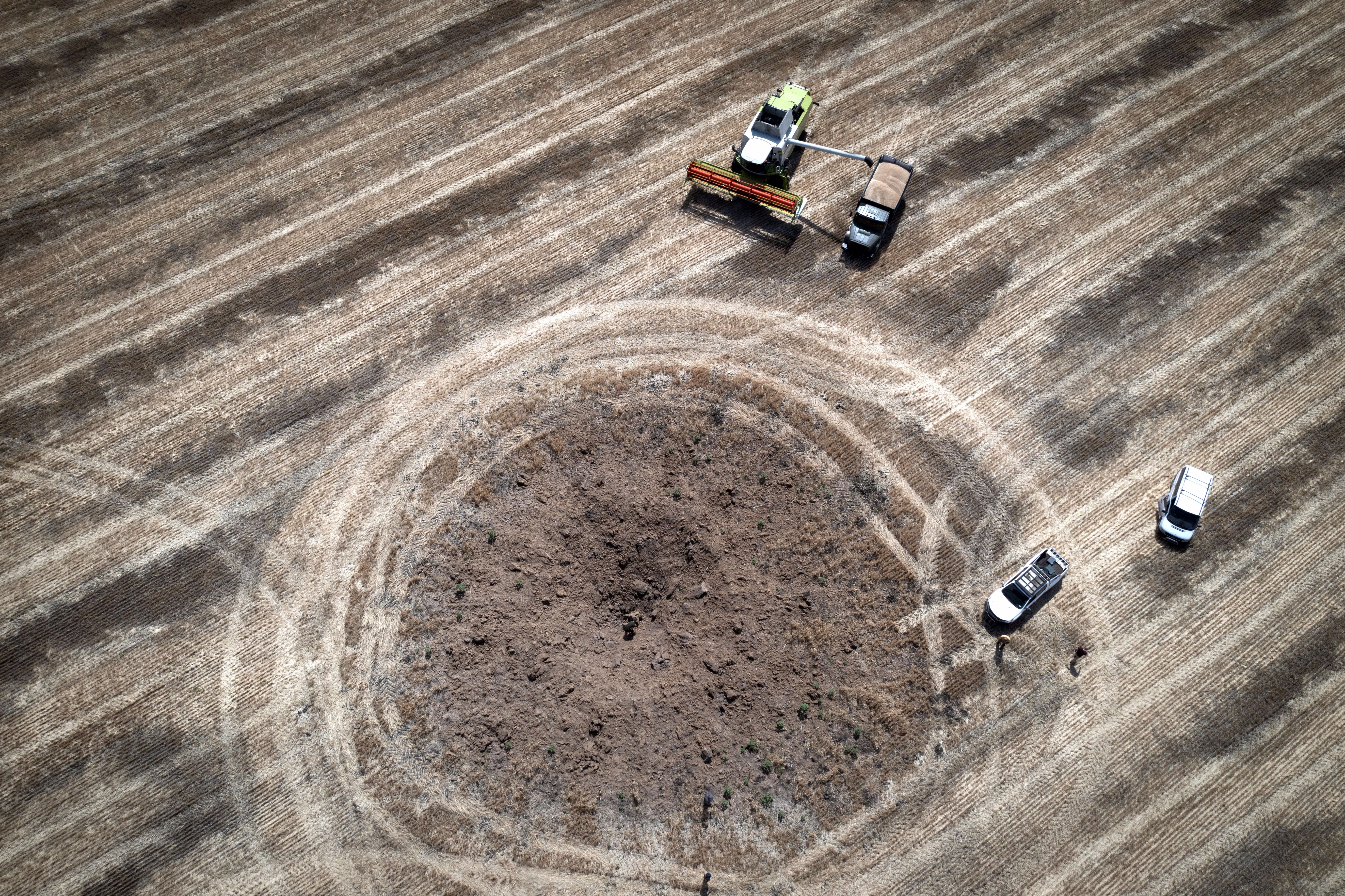 An aerial view of farm vehicles in a field near a fresh crater left by a Russian rocket.