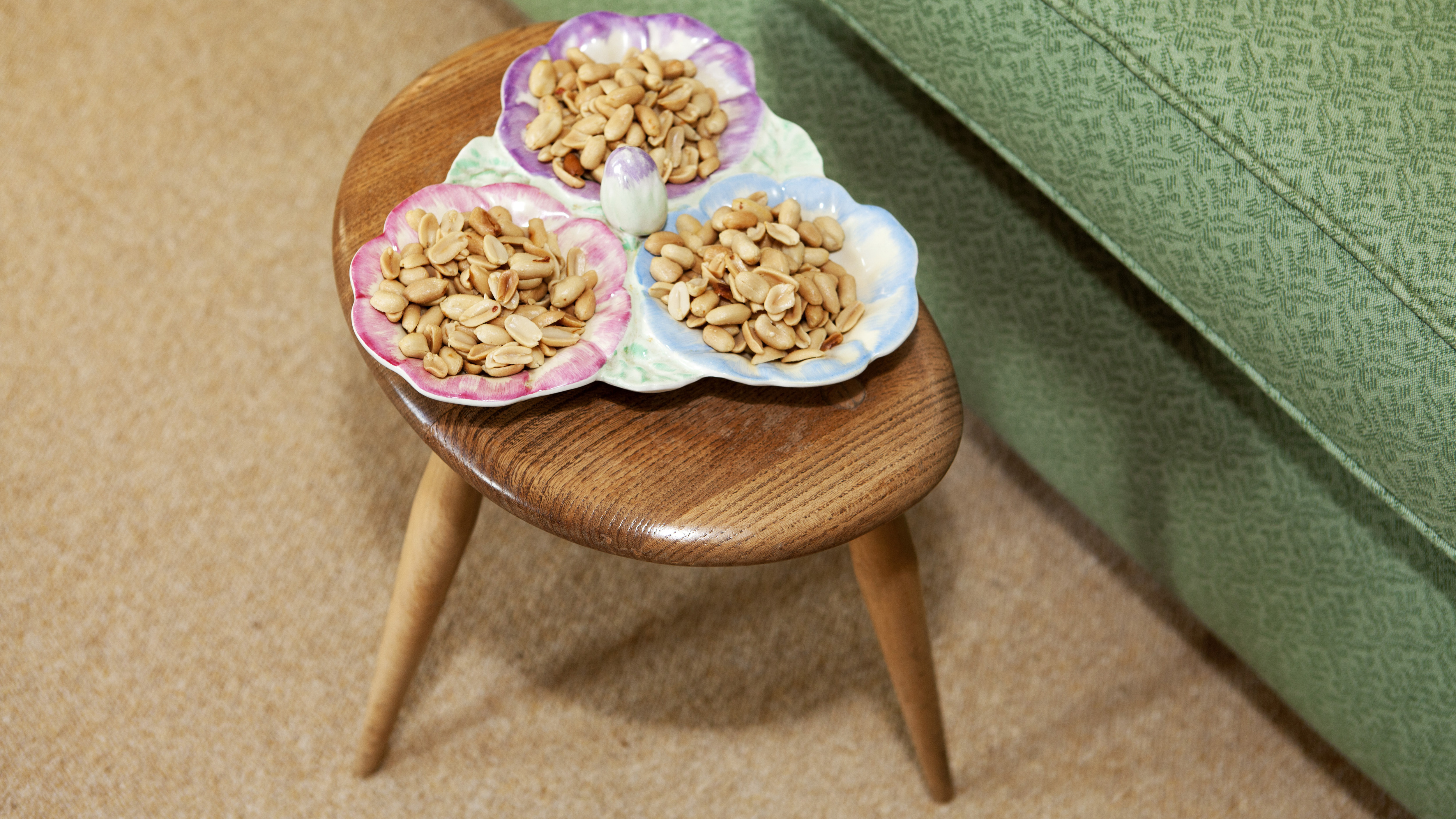A serving dish containing nuts, placed on a small wooden table, next to a couch. Inviting!