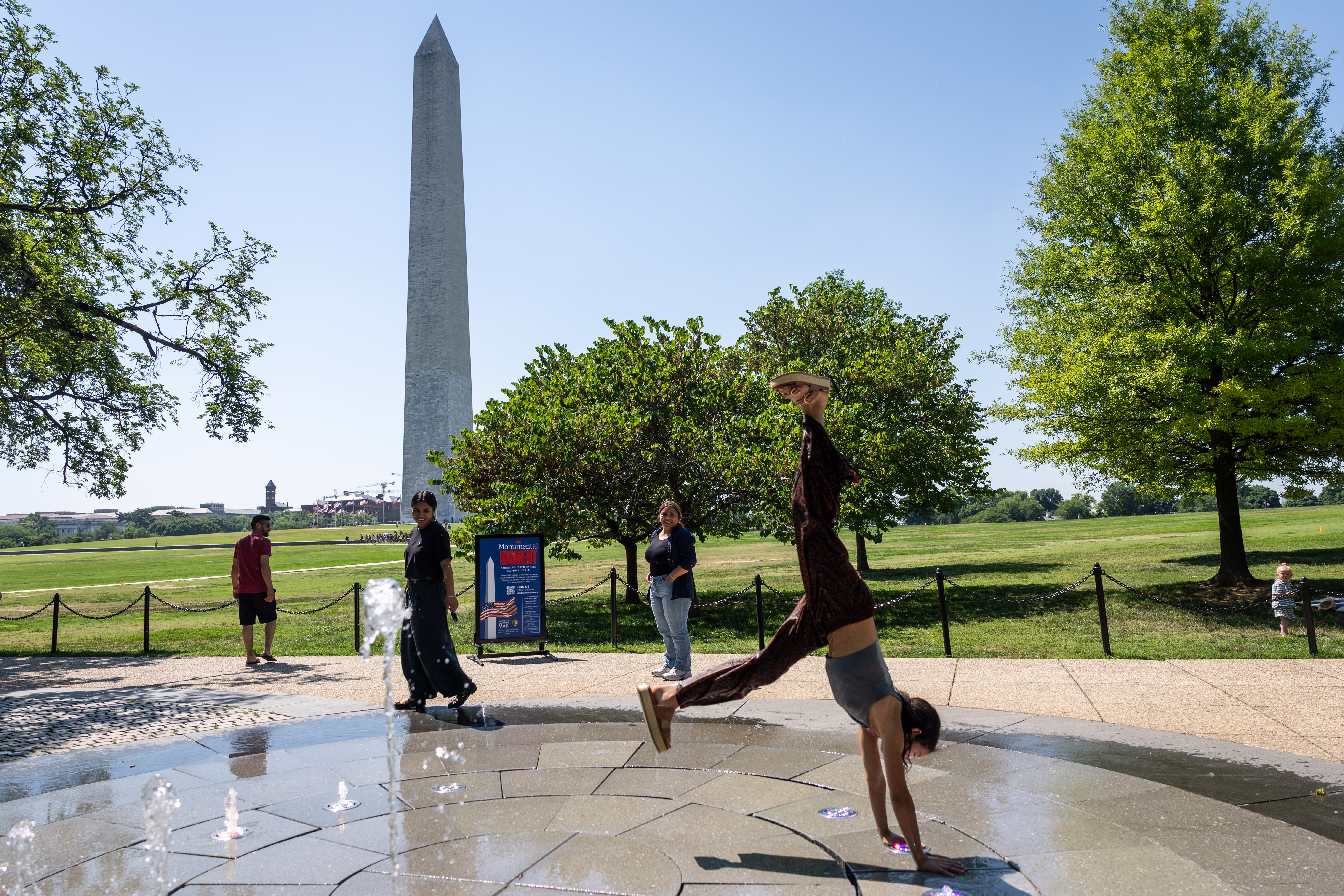 A family watches as a girl does a cartwheel near the Washington Monument.