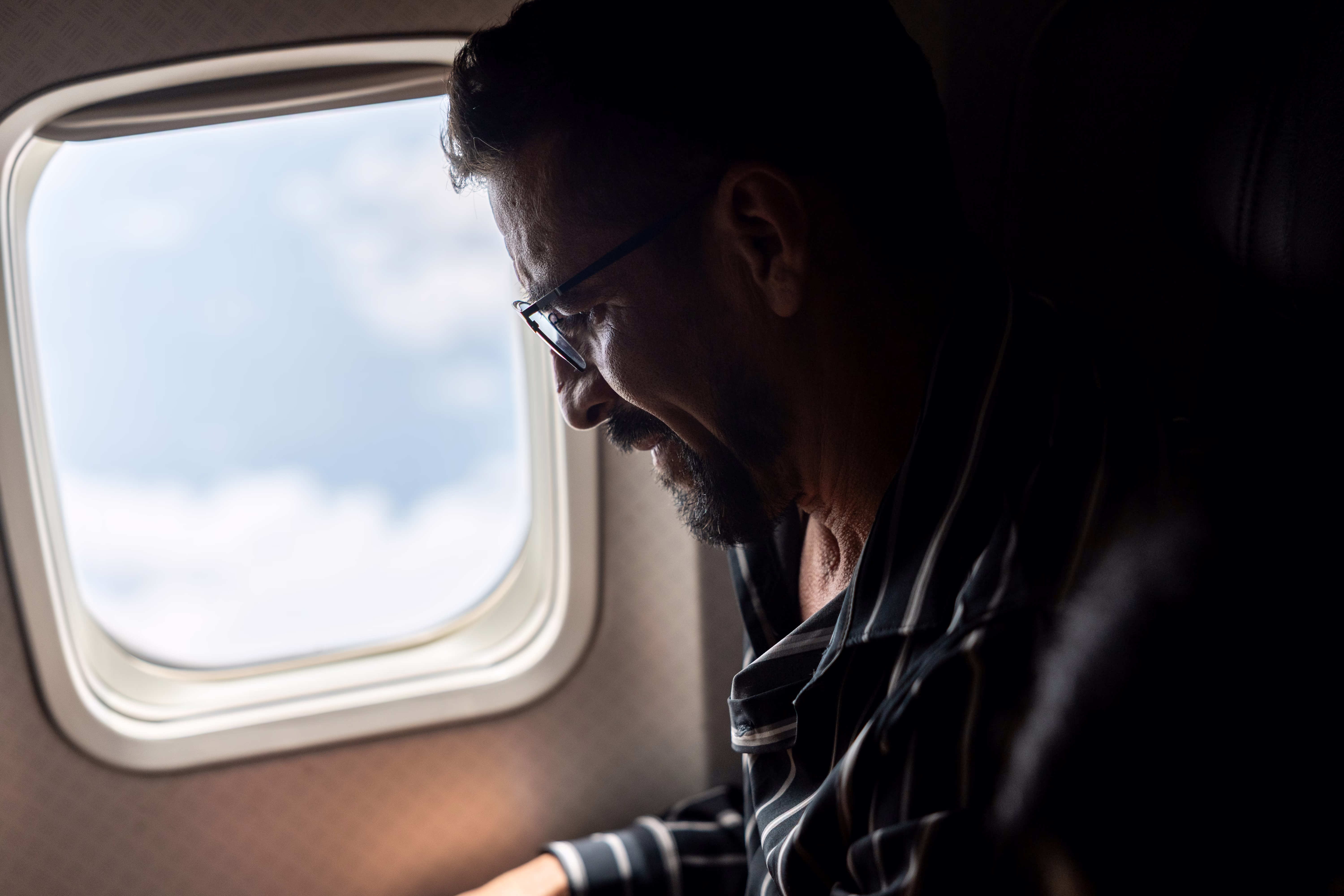A man, seated in a window seat on an airplane
