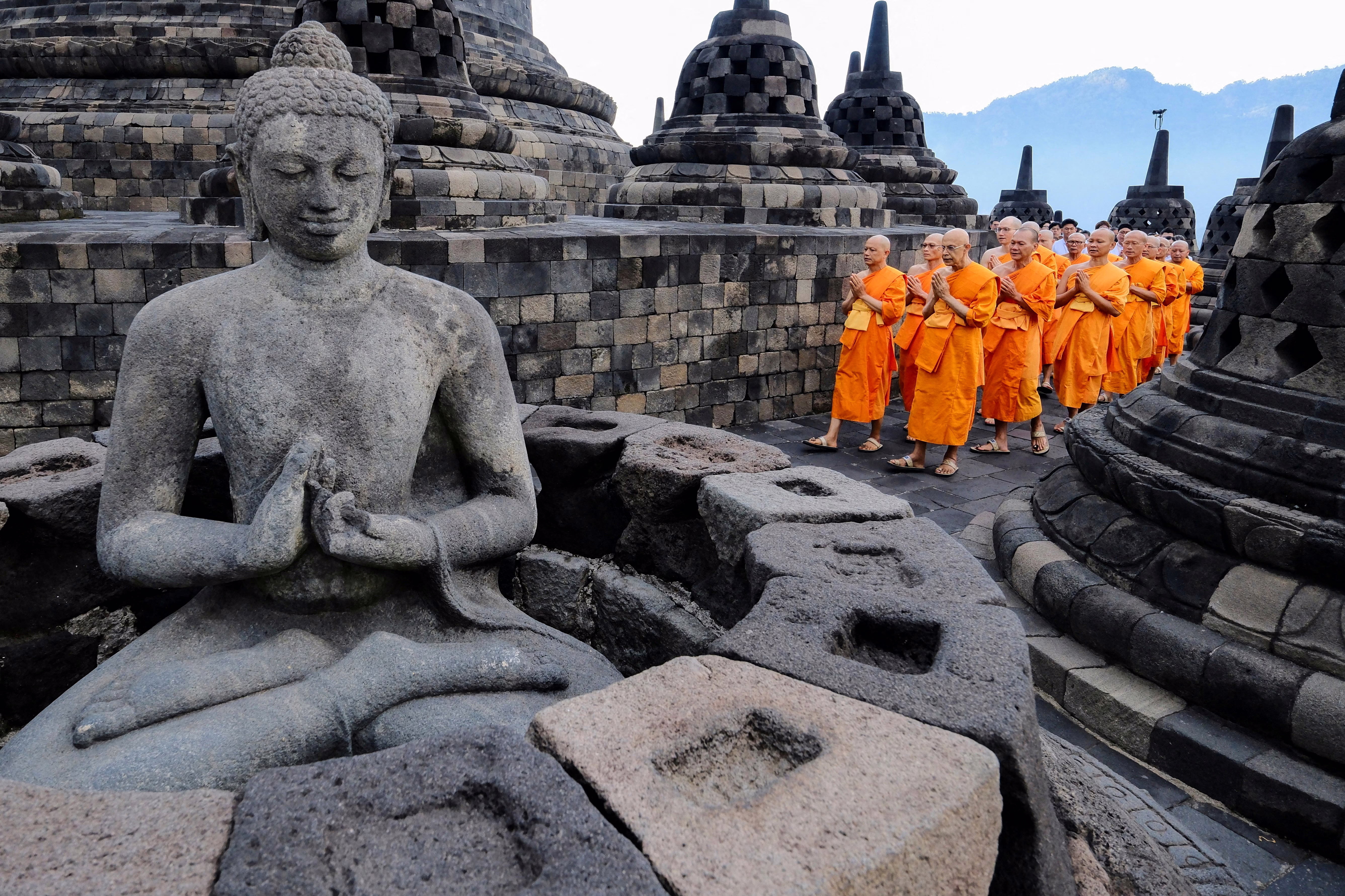 Buddhist monks walk together around a stone temple.