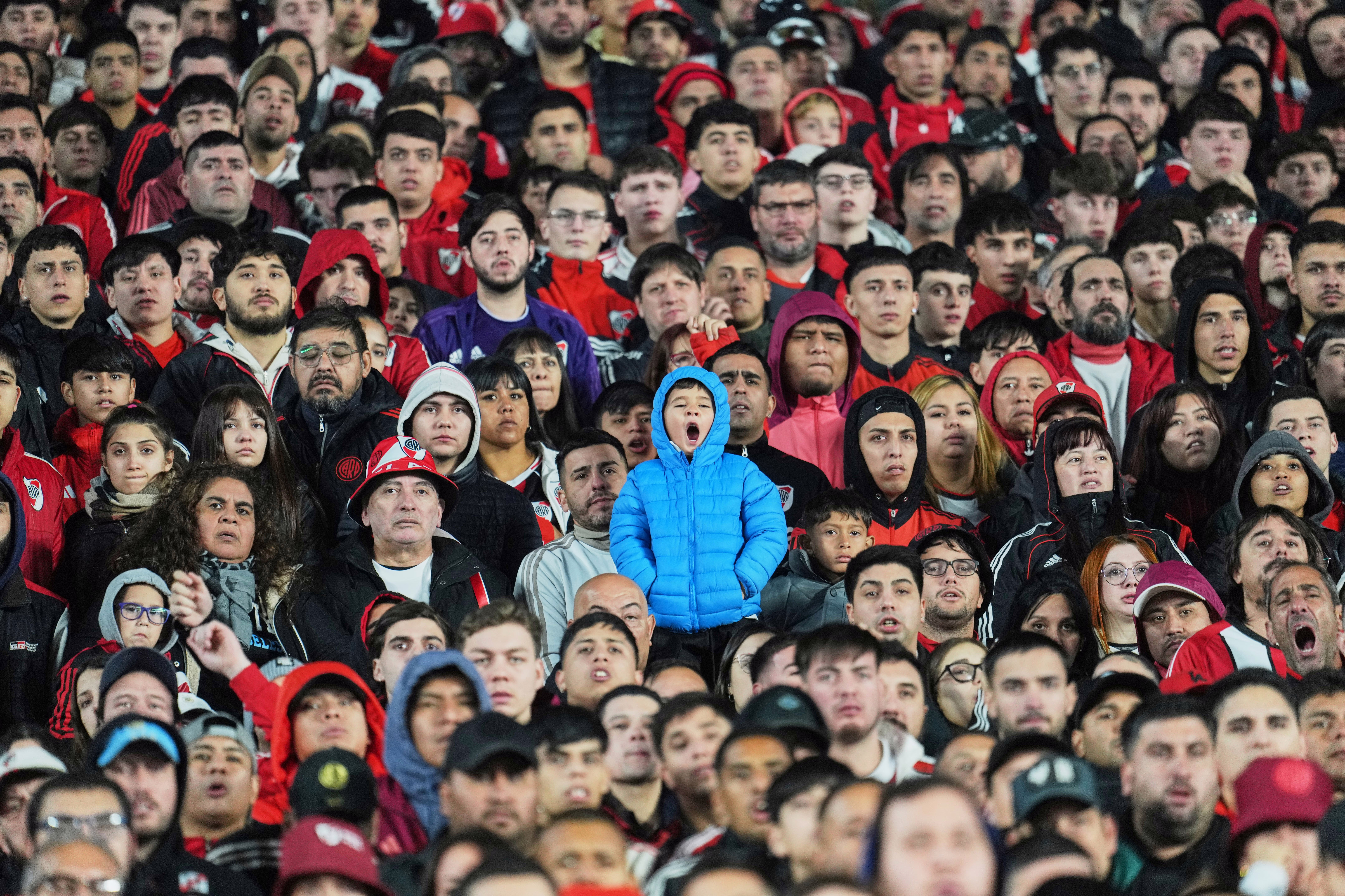 A child stands among many seated soccer fans in a stadium.
