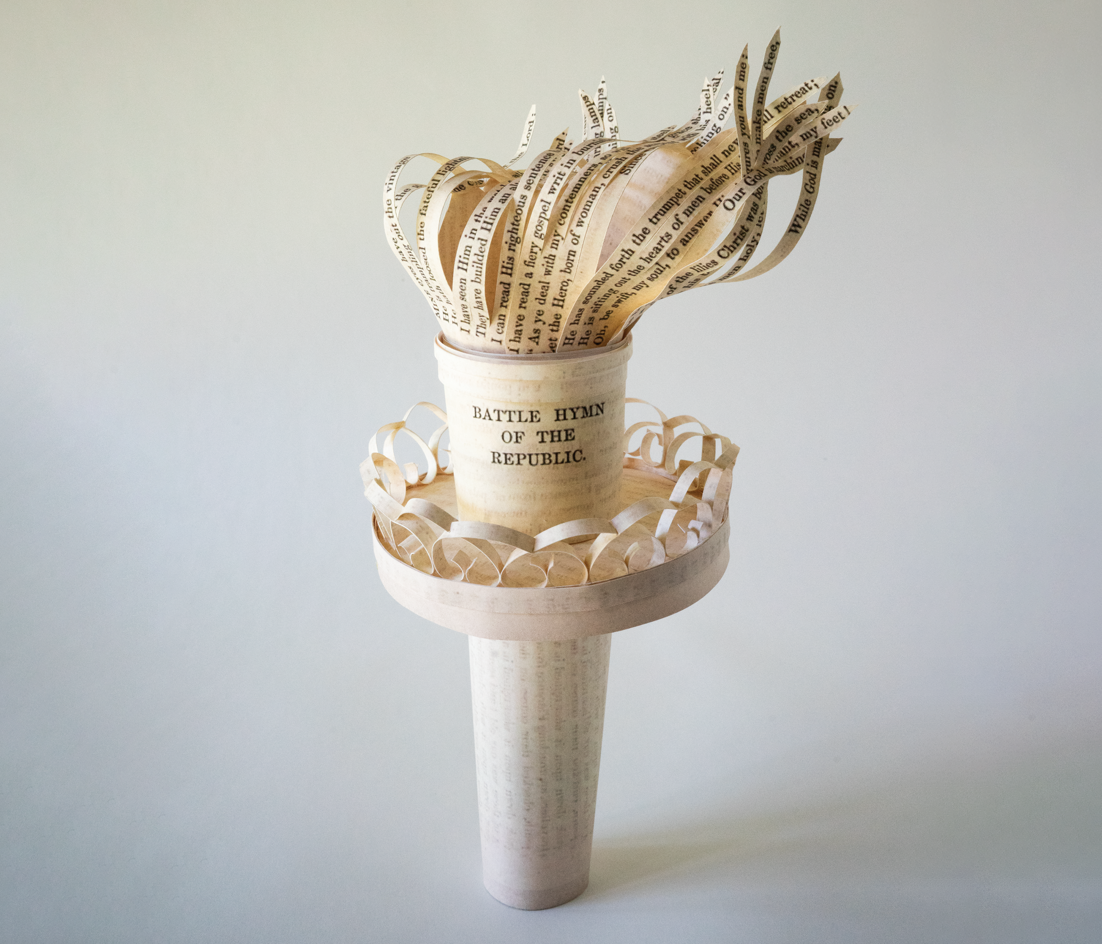 A paper sculpture of Lady Liberty's torch made of strips of the printed “Battle Hymn of the Republic,” with the lines of the poem forming the flames.