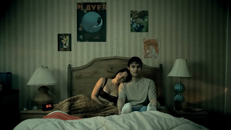 A girl rests her head on a boy's shoulder while they are sitting in bed