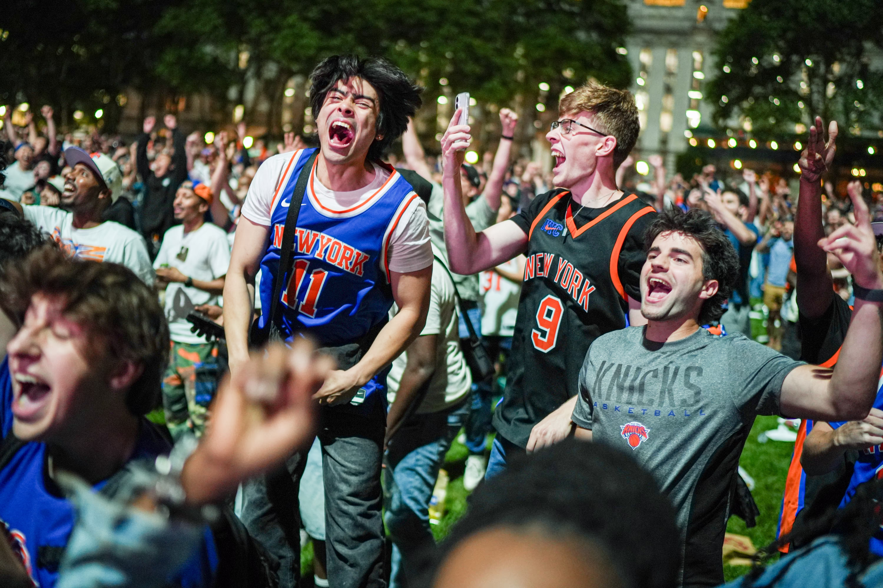 New York Knicks fans cheer at a watch party in a park.