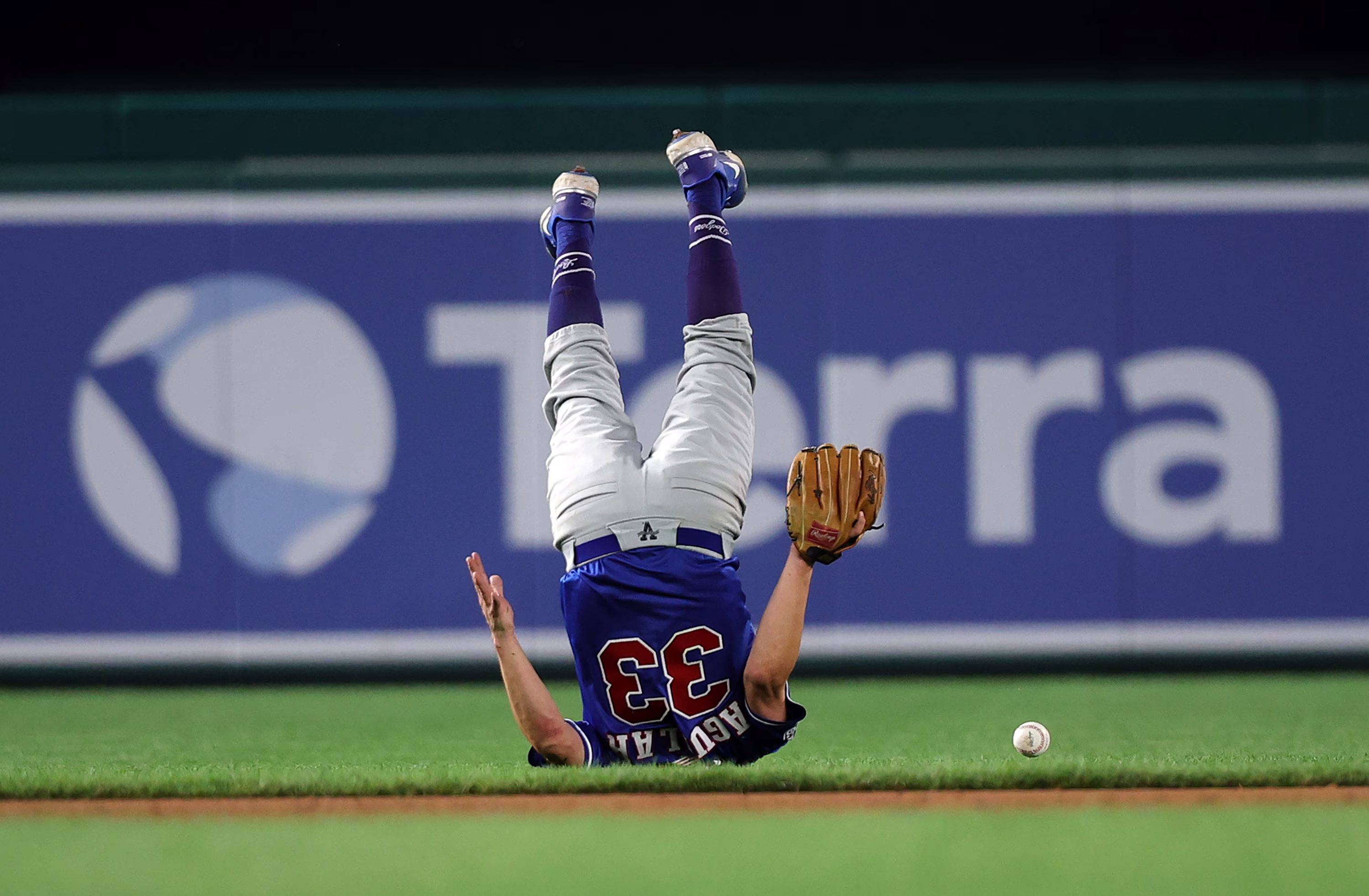 A person wearing a baseball uniform, upside down, tumbling after a ball