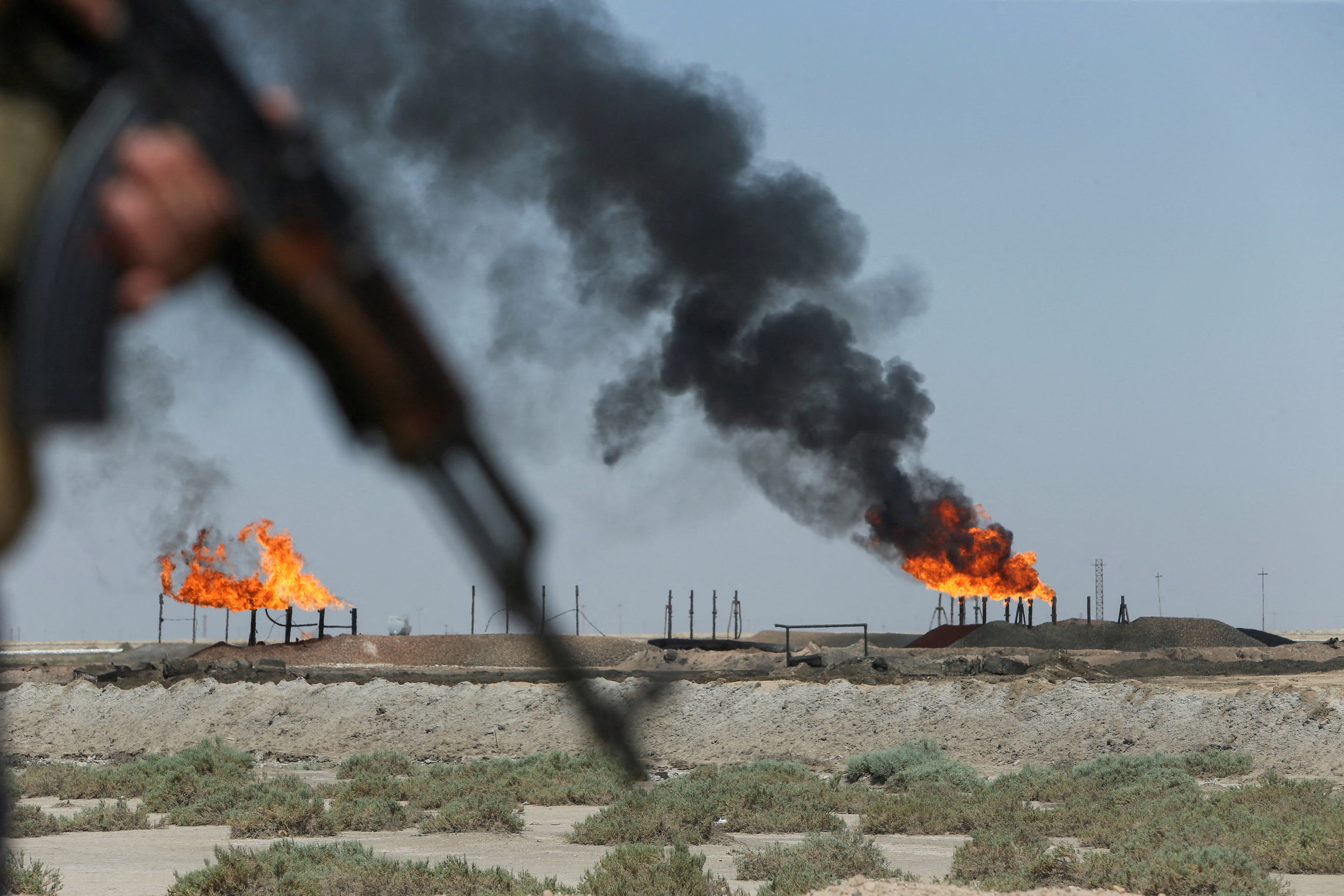 Gas flares burn at an oil field as an armed police officer stands nearby.
