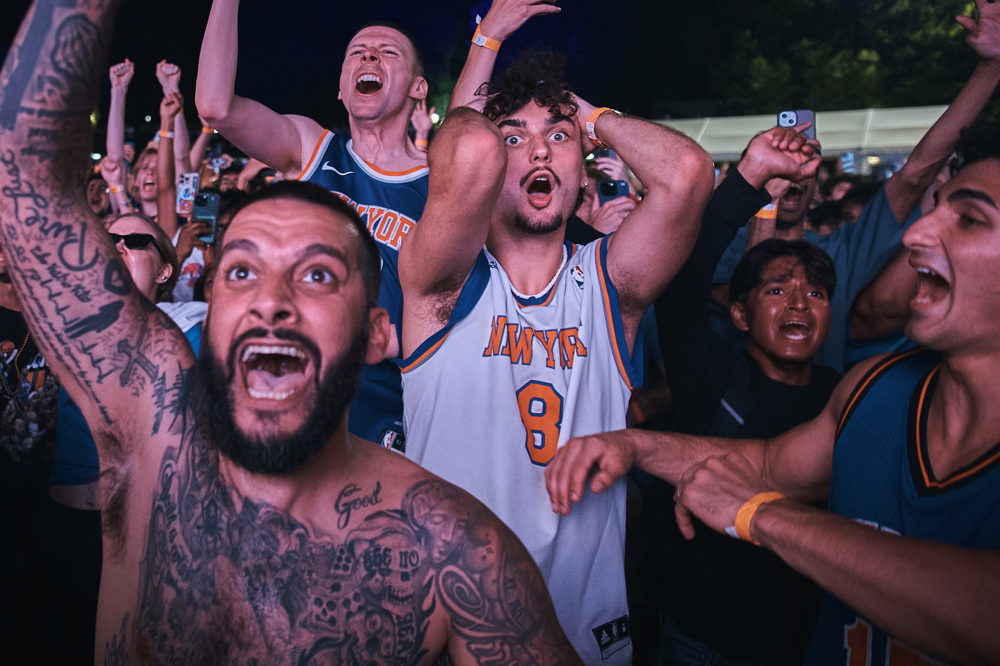 A group of basketball fans at a watch party cheer and raise their arms.