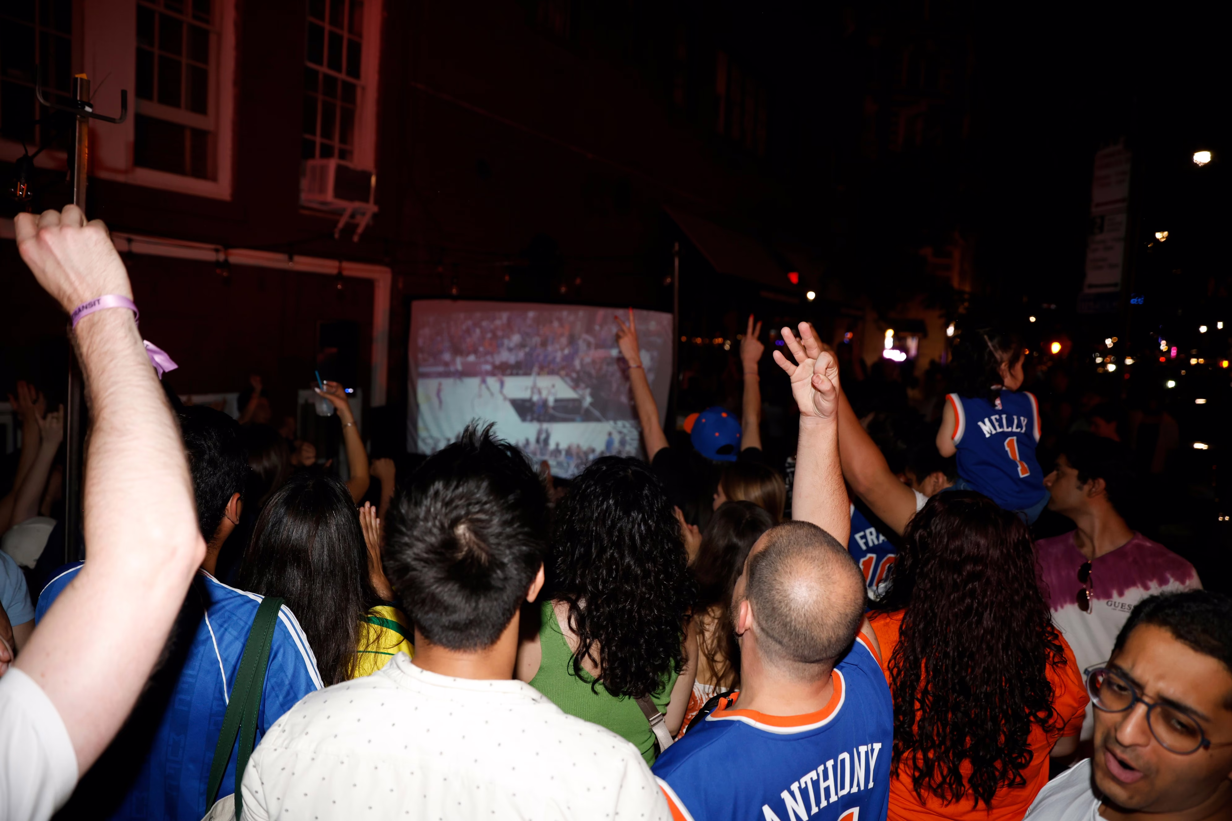 Knicks fans attend a watch party, viewing the game projected on a screen outside.