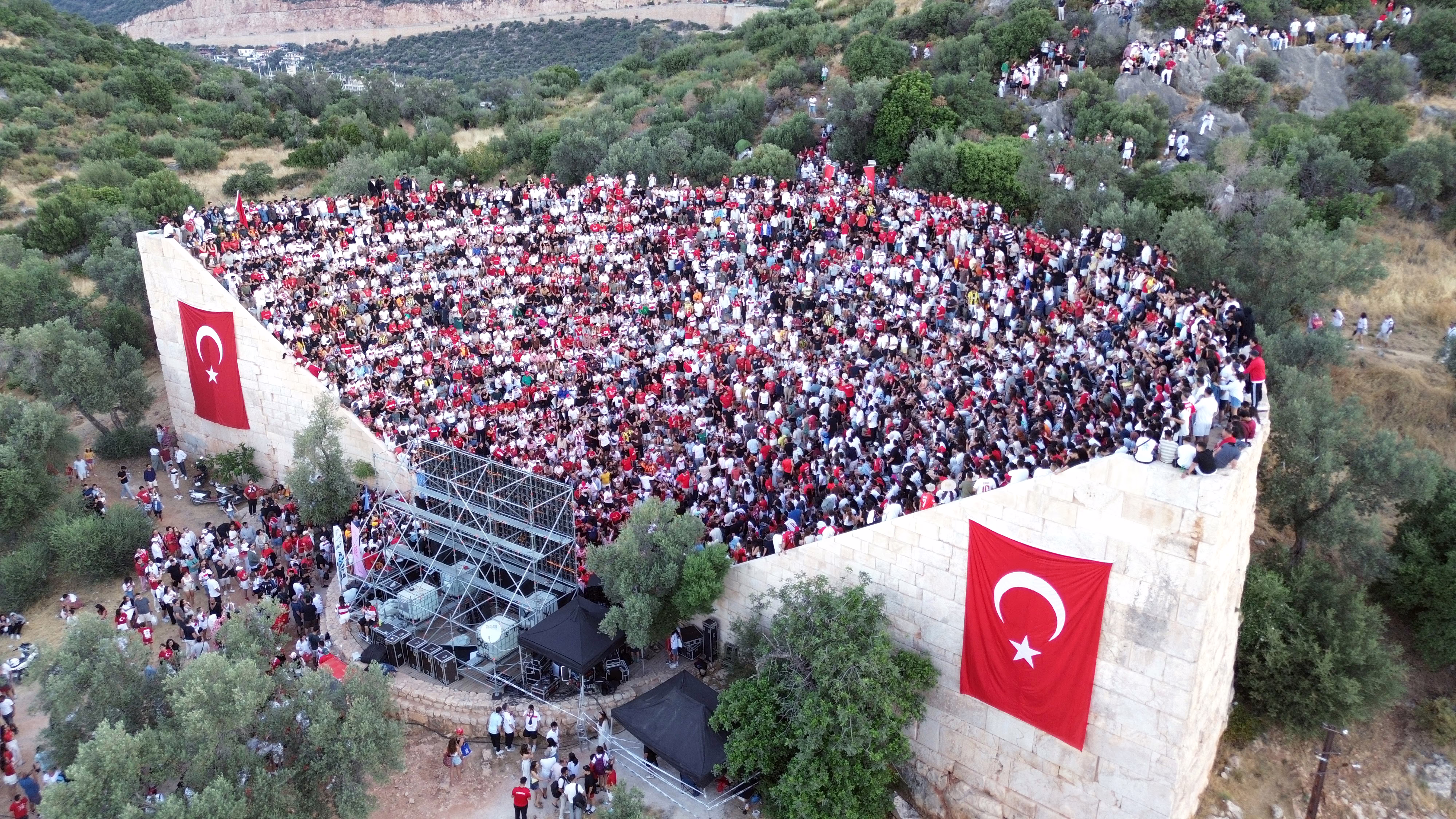 An aerial view of football fans gathered in an ancient outdoor amphitheater in Turkey, where they watch a game on a big screen