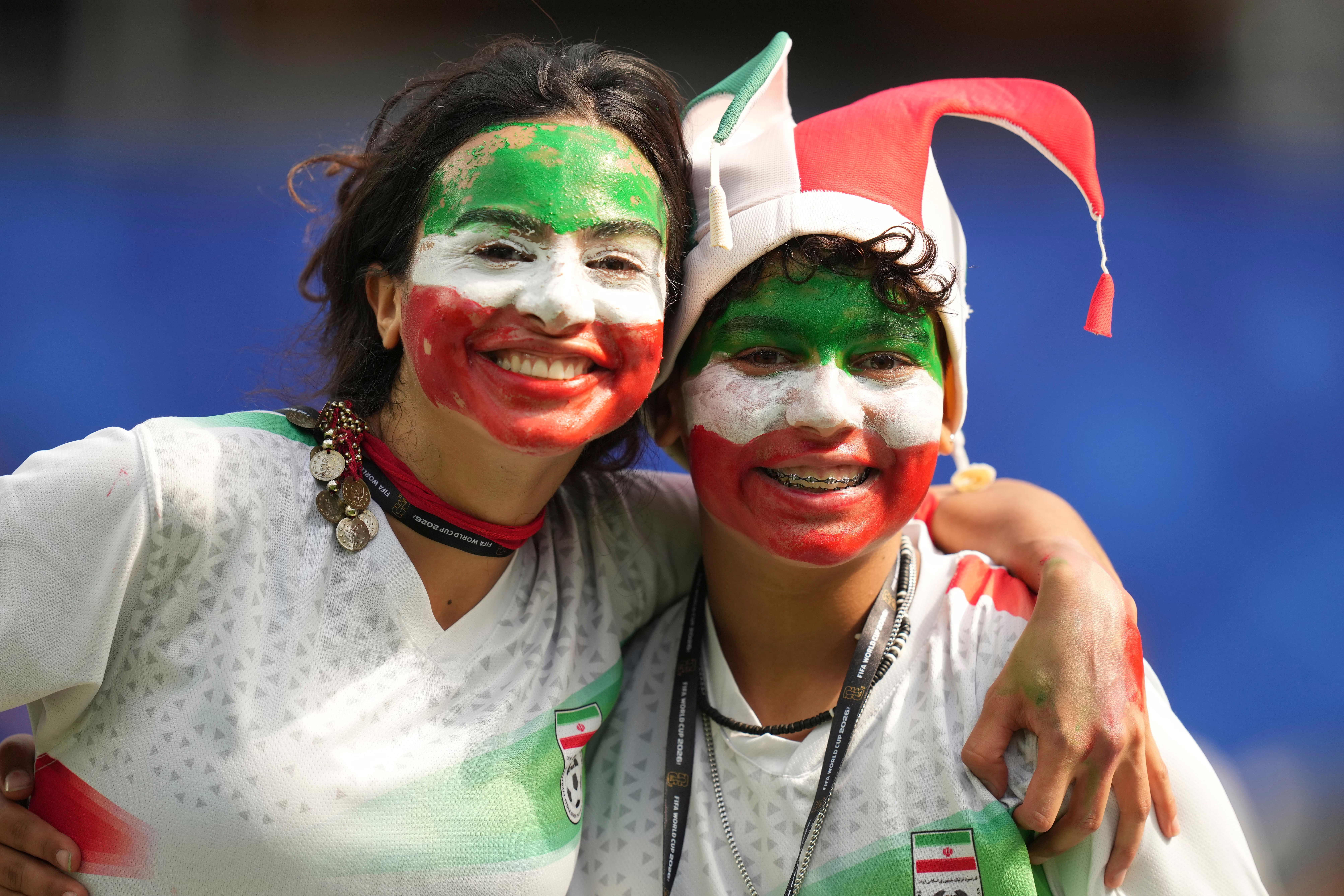 Fans of Team Iran, with the colors of Iran's flag painted on their faces, smile for the camera.