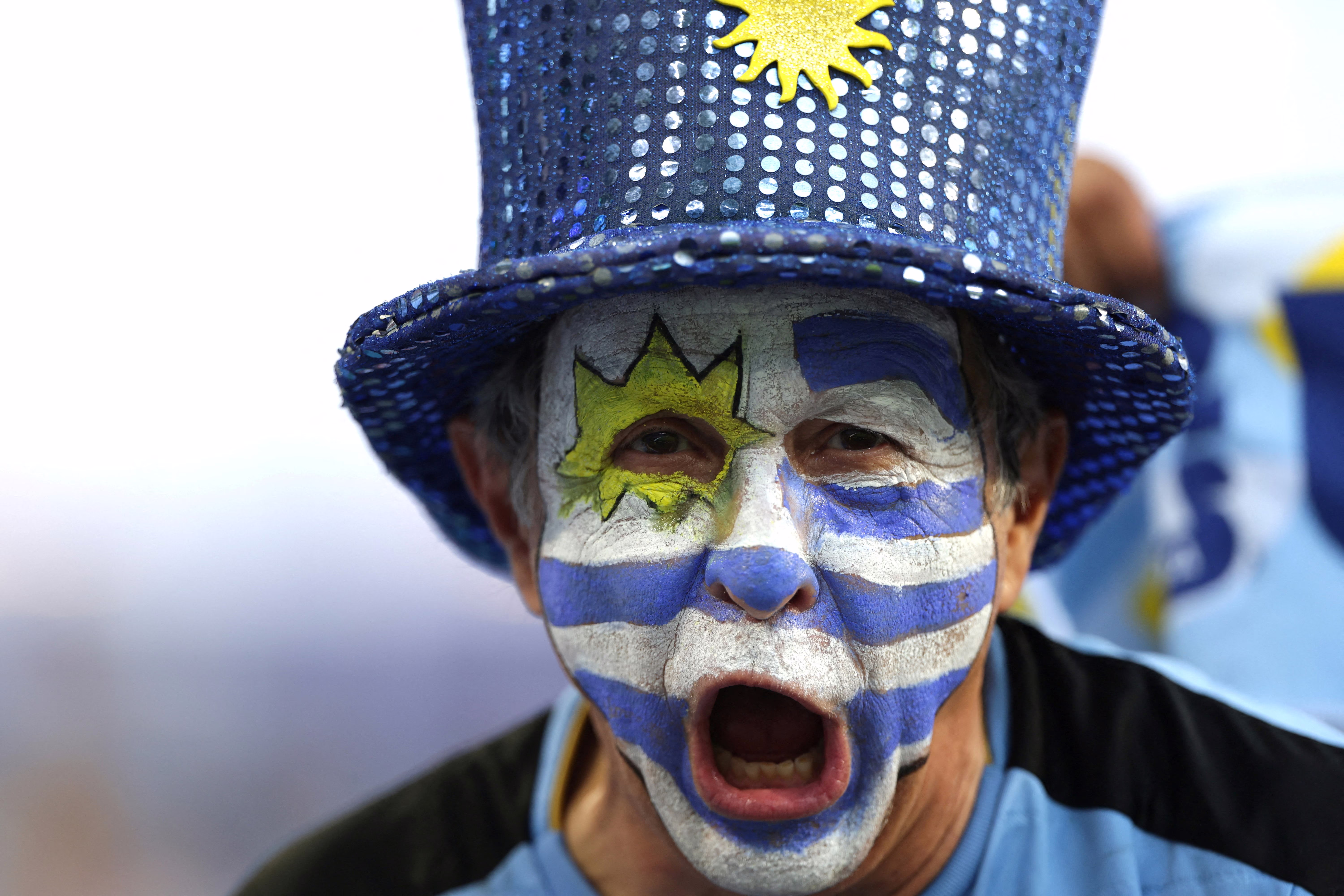 A soccer fan with the flag of Uruguay painted on their face cheers before a match.