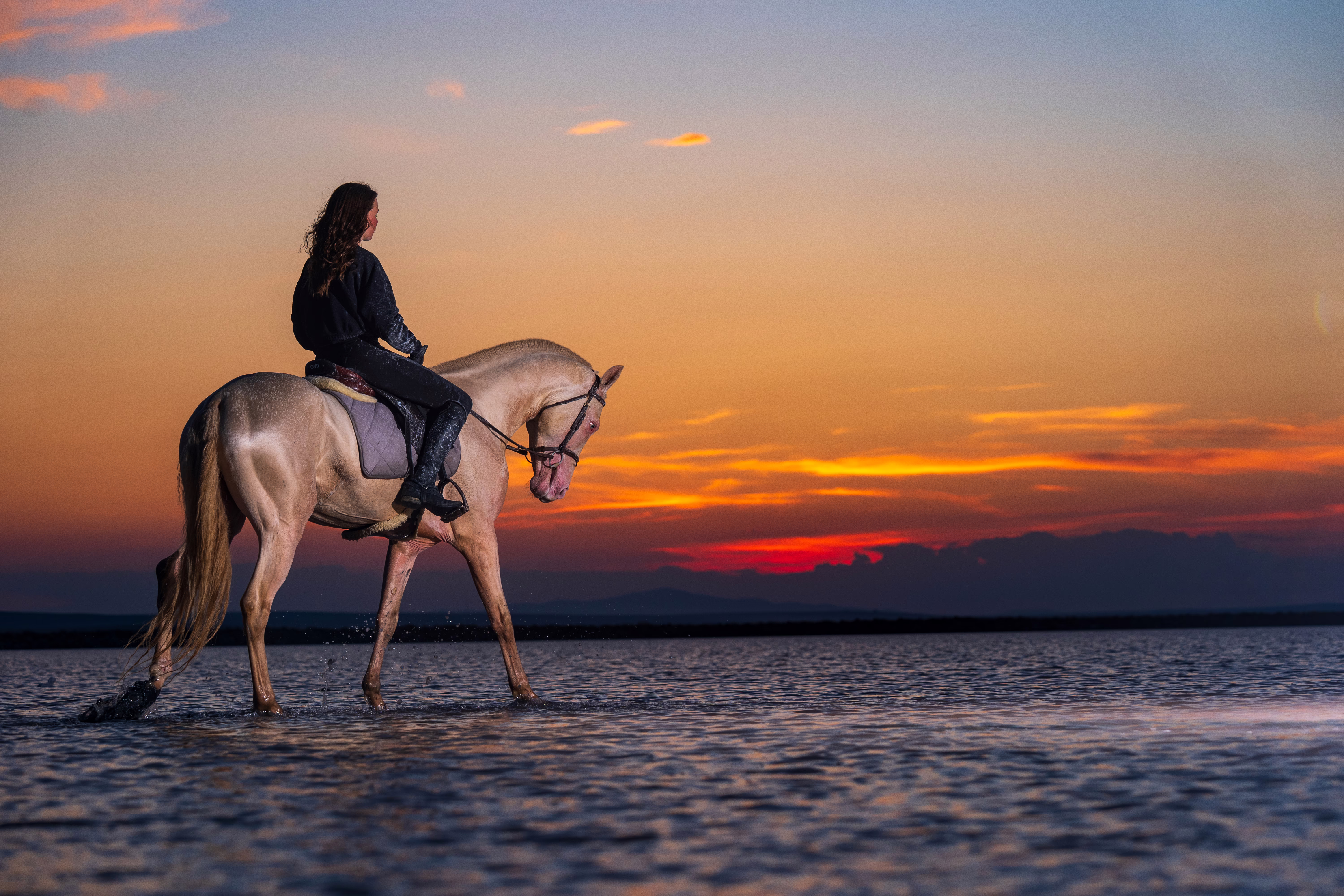 A woman rides a horse in very shallow water at sunset.