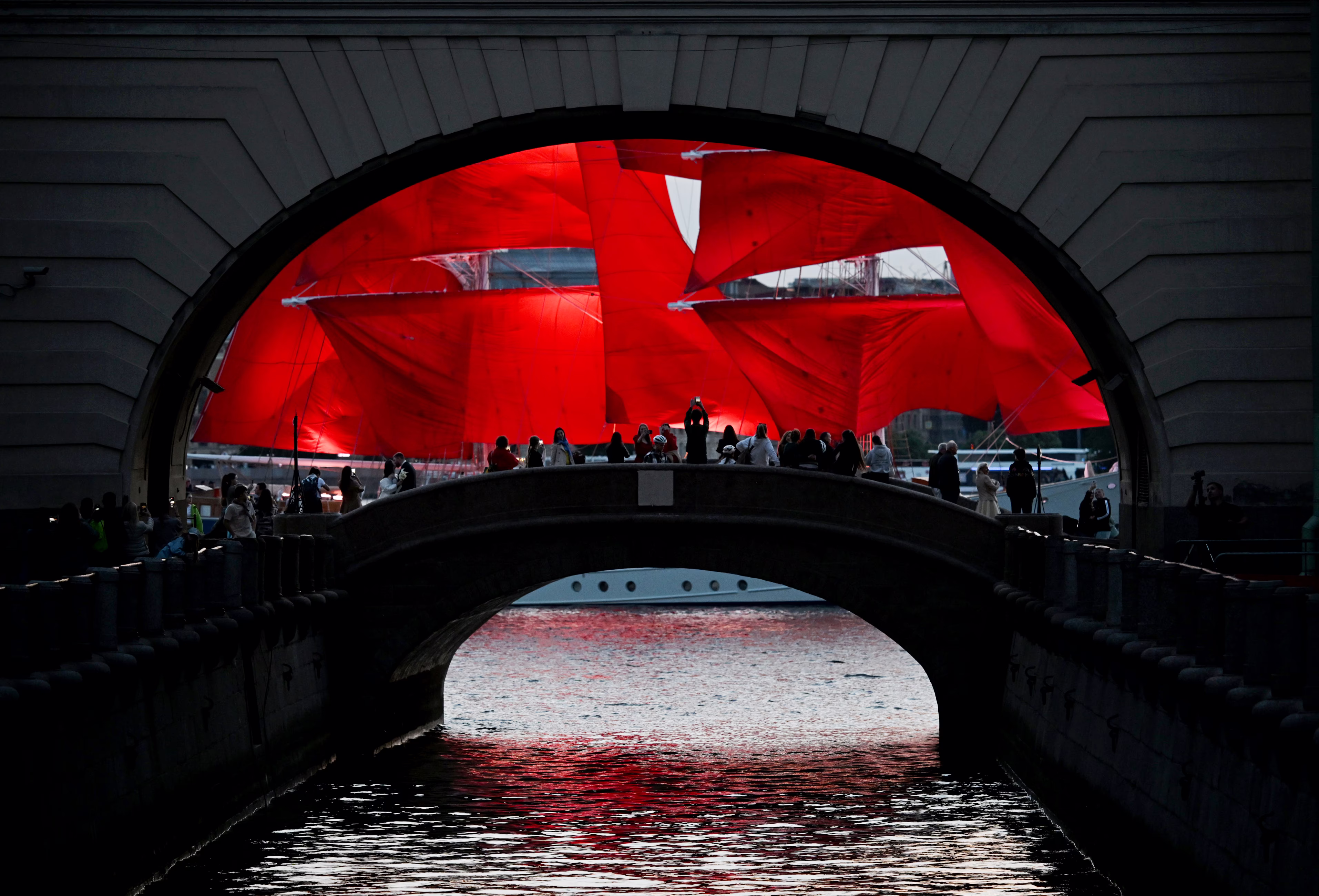 A tall sailing ship with red sails passes by an archway.