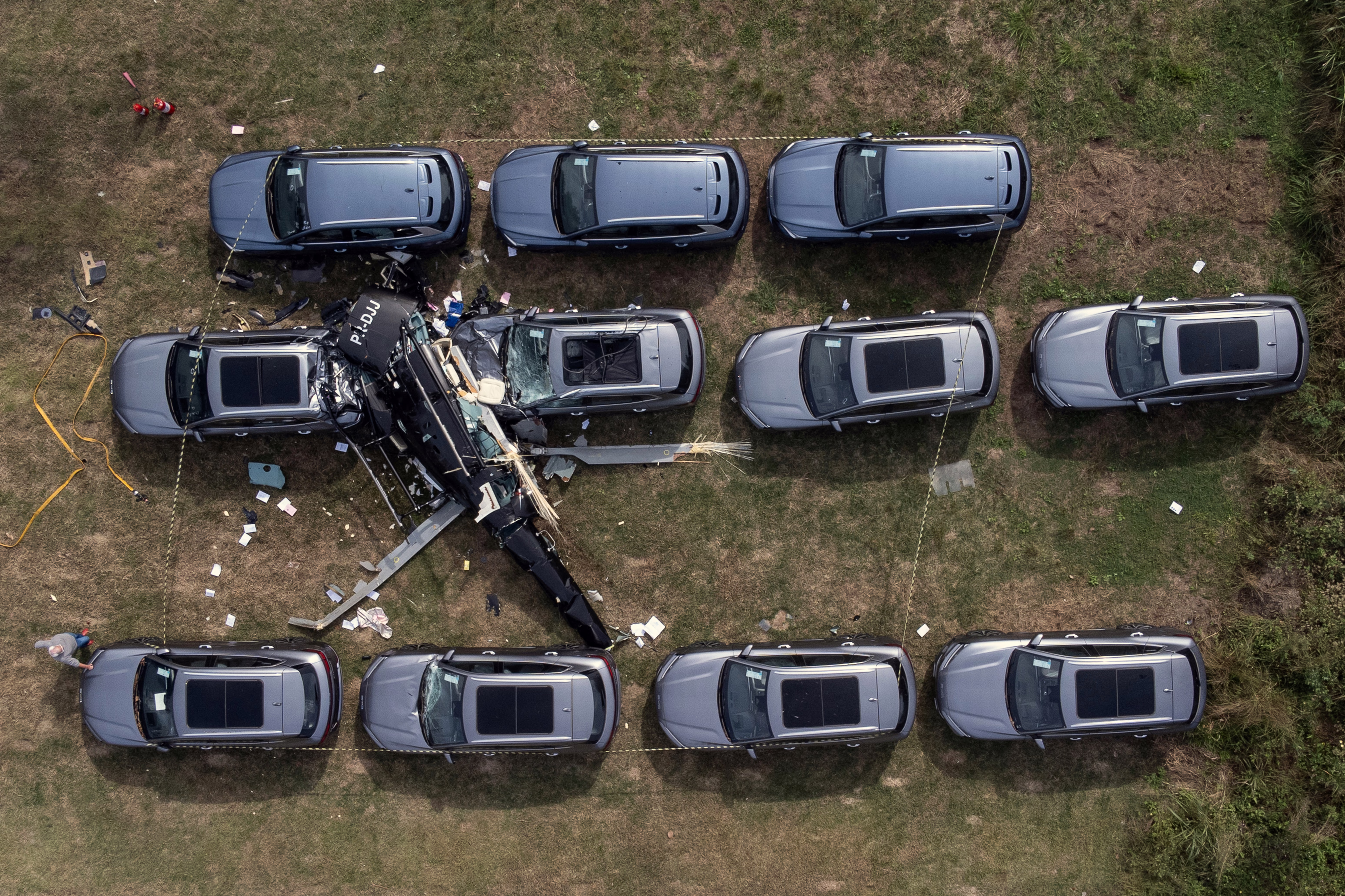 An aerial view of a crashed helicopter lying on top of several new cars. 