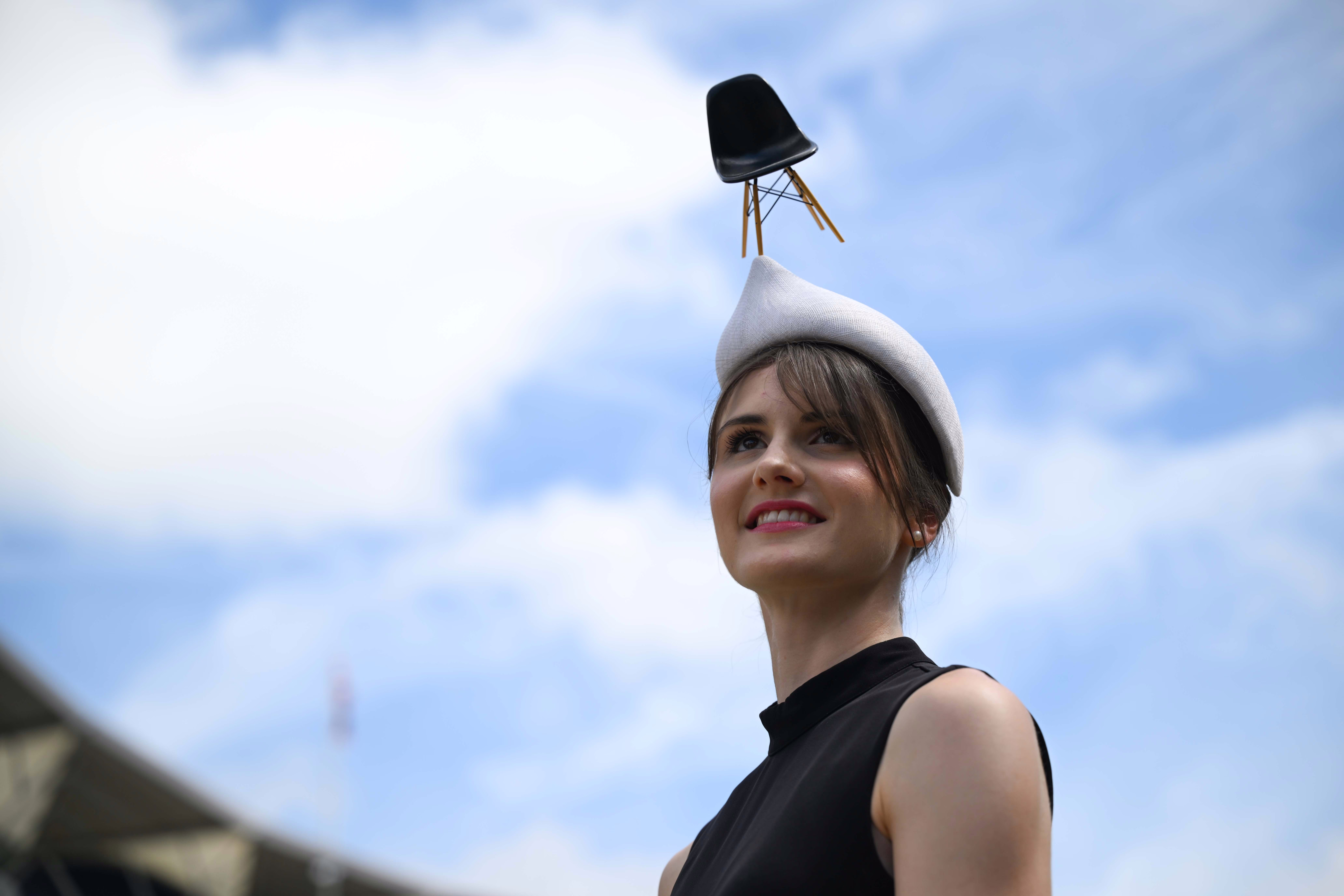 A person poses for a photo, wearing a fashionable cap with a tiny chair attached to the top of it.