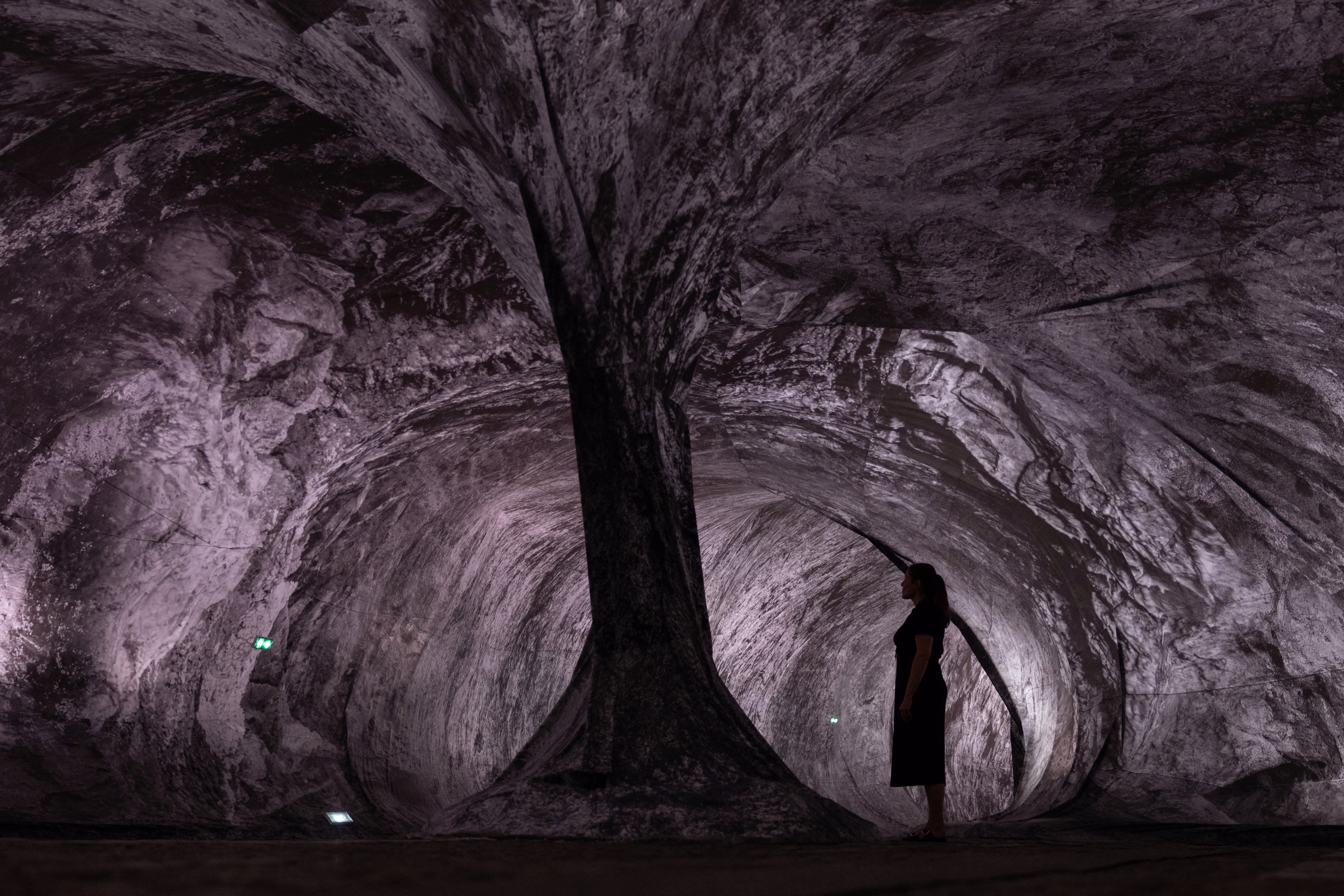 A person stands inside an art exhibit, looking up, appearing as if they were in a cave.