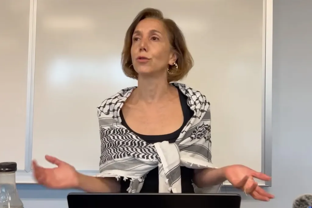 Corinna Mullin speaking while wearing a Palestinian keffiyeh.