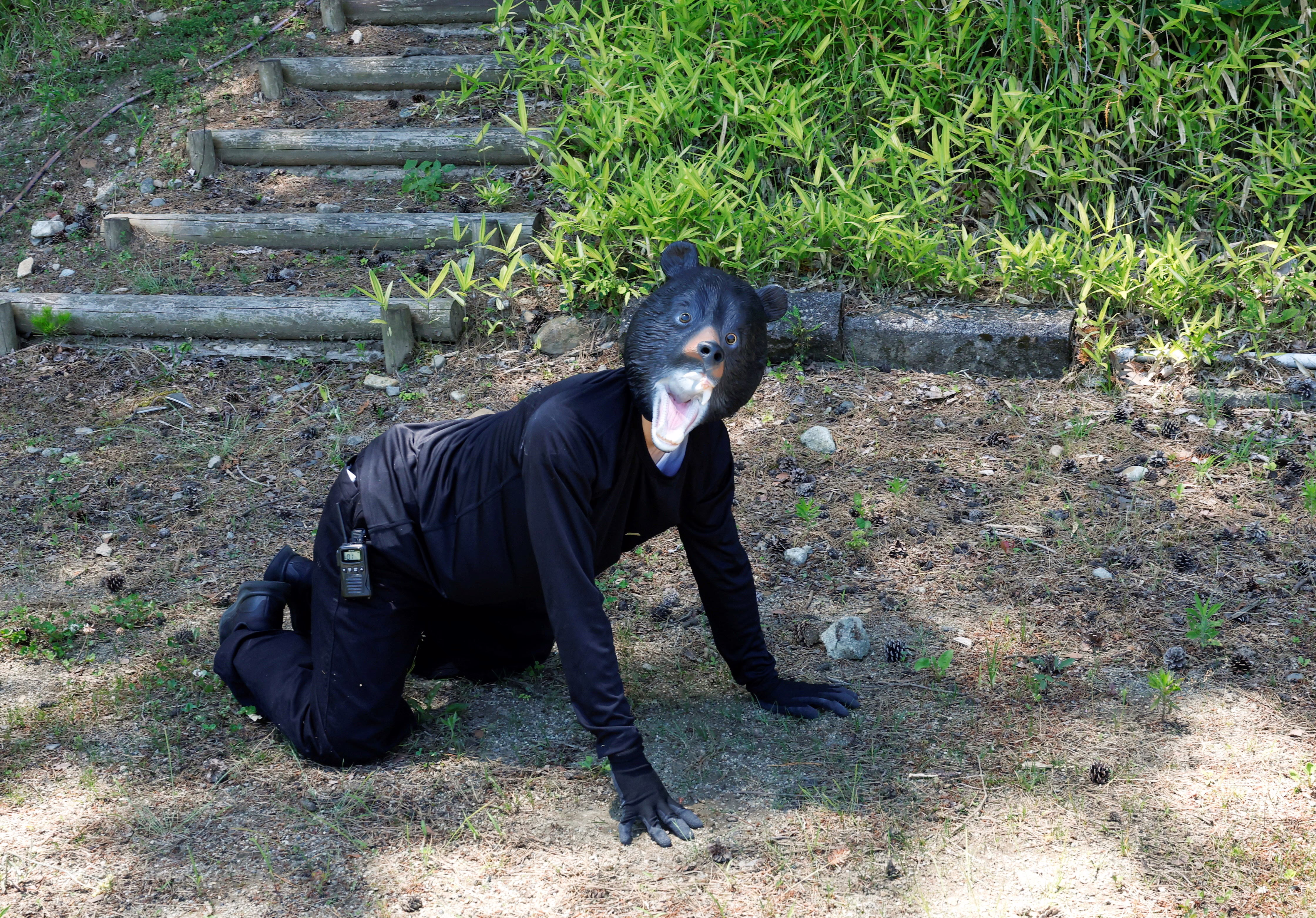 A man in a bear mask and dark clothing, on all fours, near a path