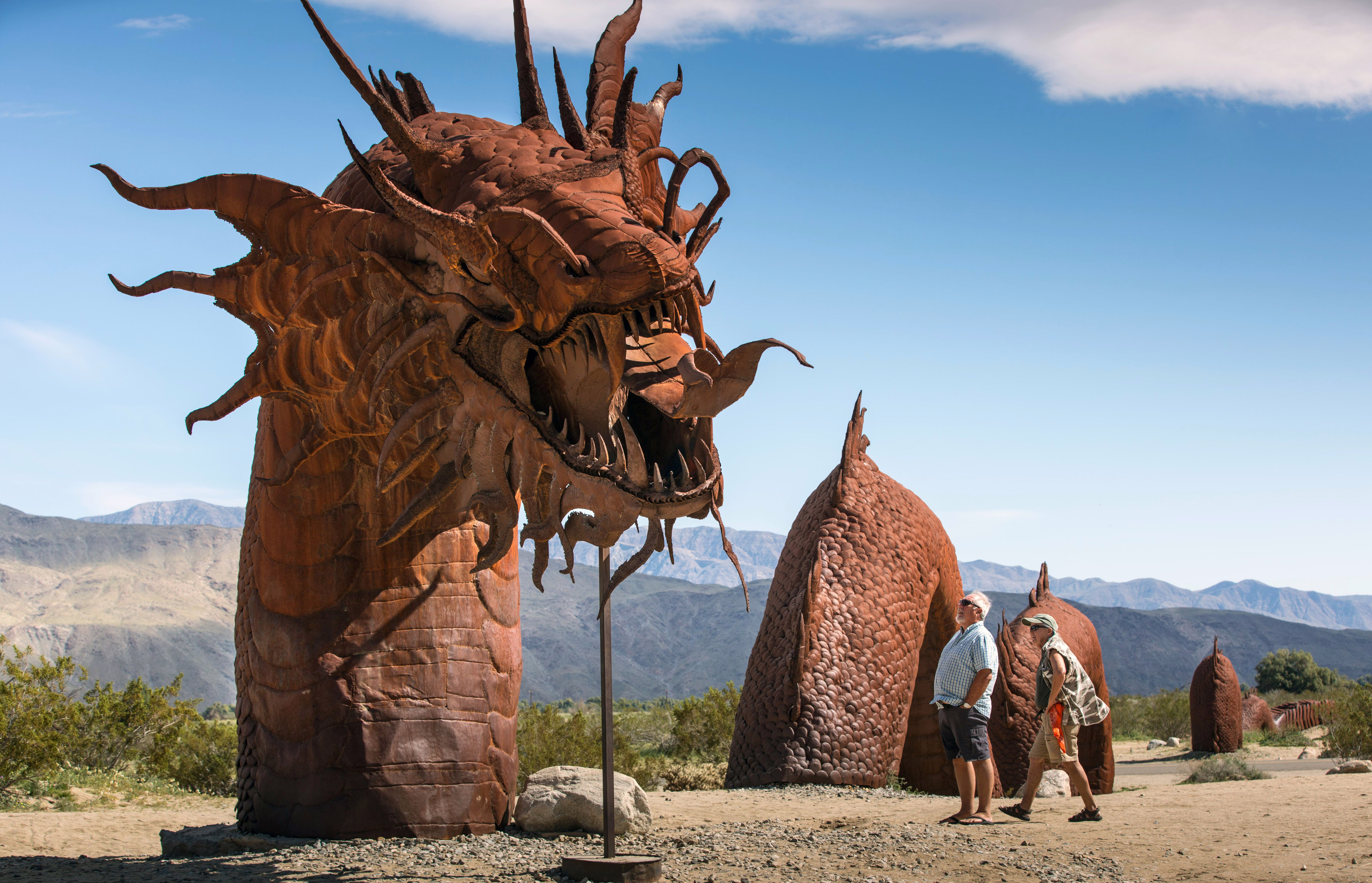People look at a large and rusting metal sculpture of a dragon.