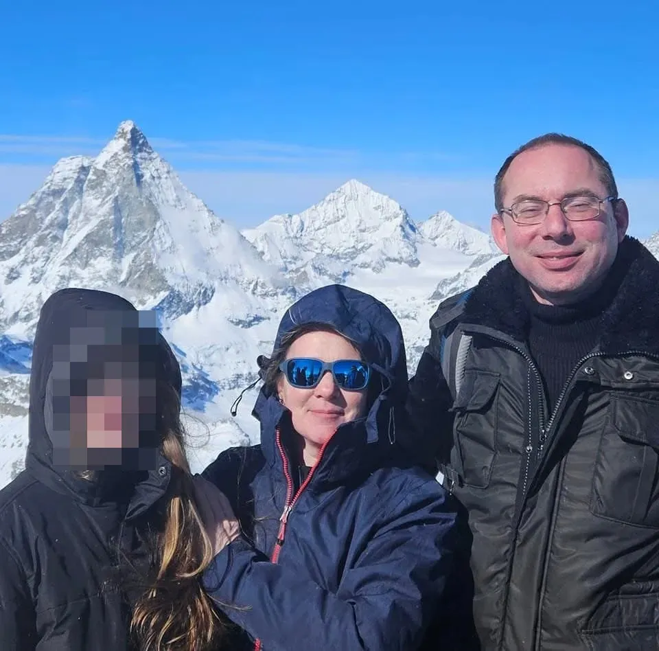 The family of Johan and Mathilda from Meerstad, with their daughter's face blurred, posing outdoors in winter clothing in front of snow-capped mountains.