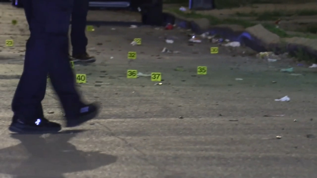 Police investigating a crime scene marked with yellow evidence markers on the ground.