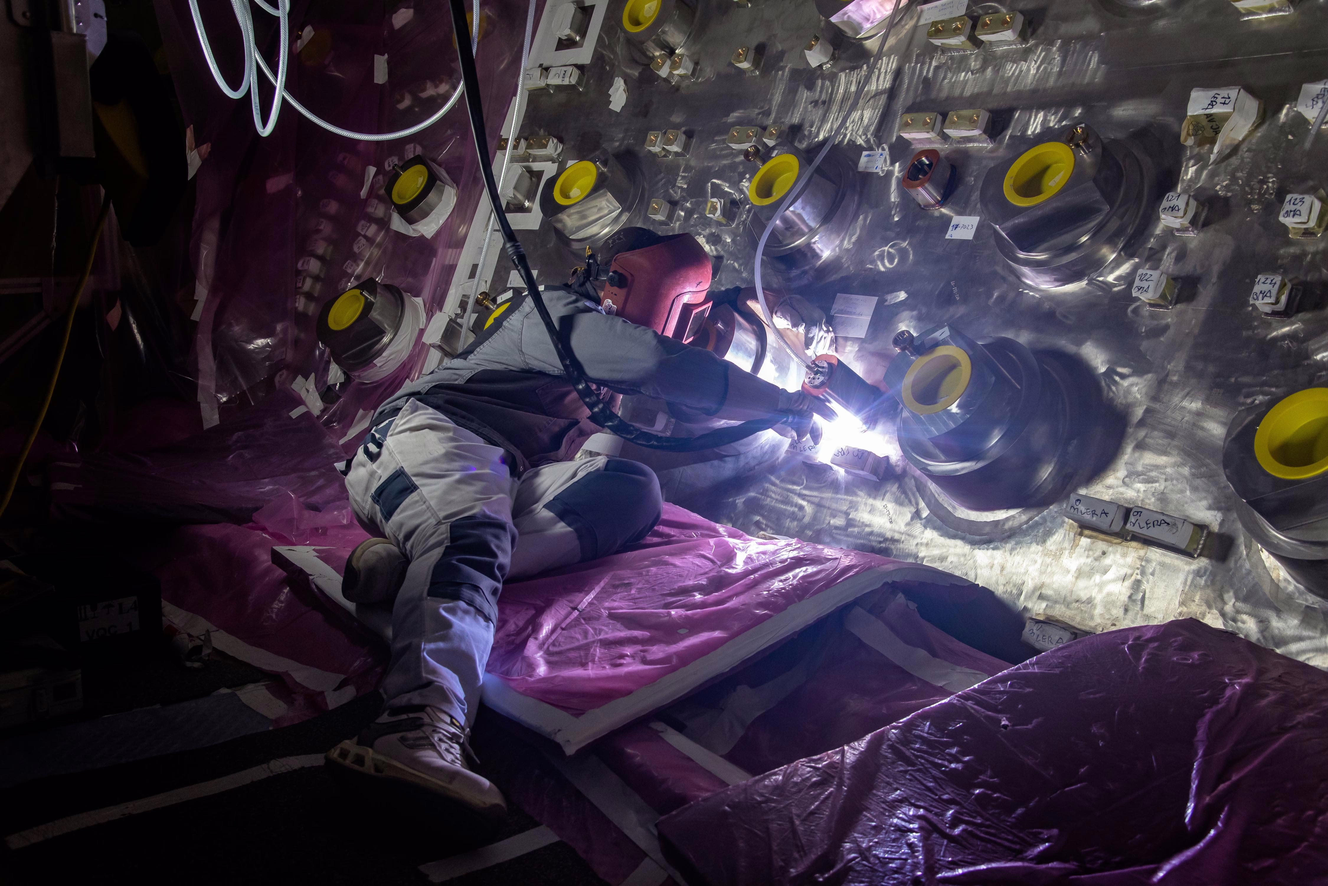 A worker welds an object onto the interior wall of a fusion reactor component.