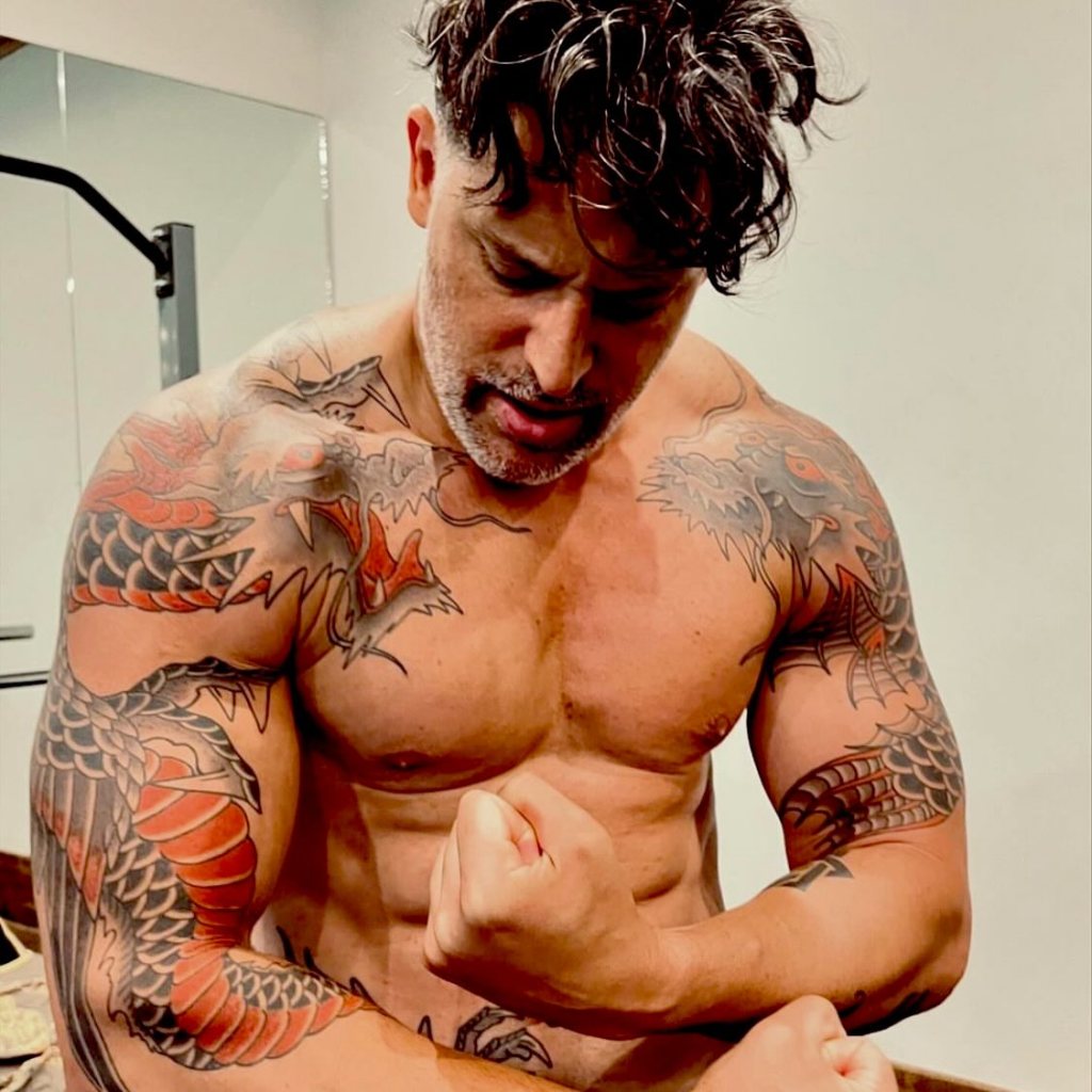 Joe Manganiello flexing his biceps with dragon tattoos on his arms and chest.