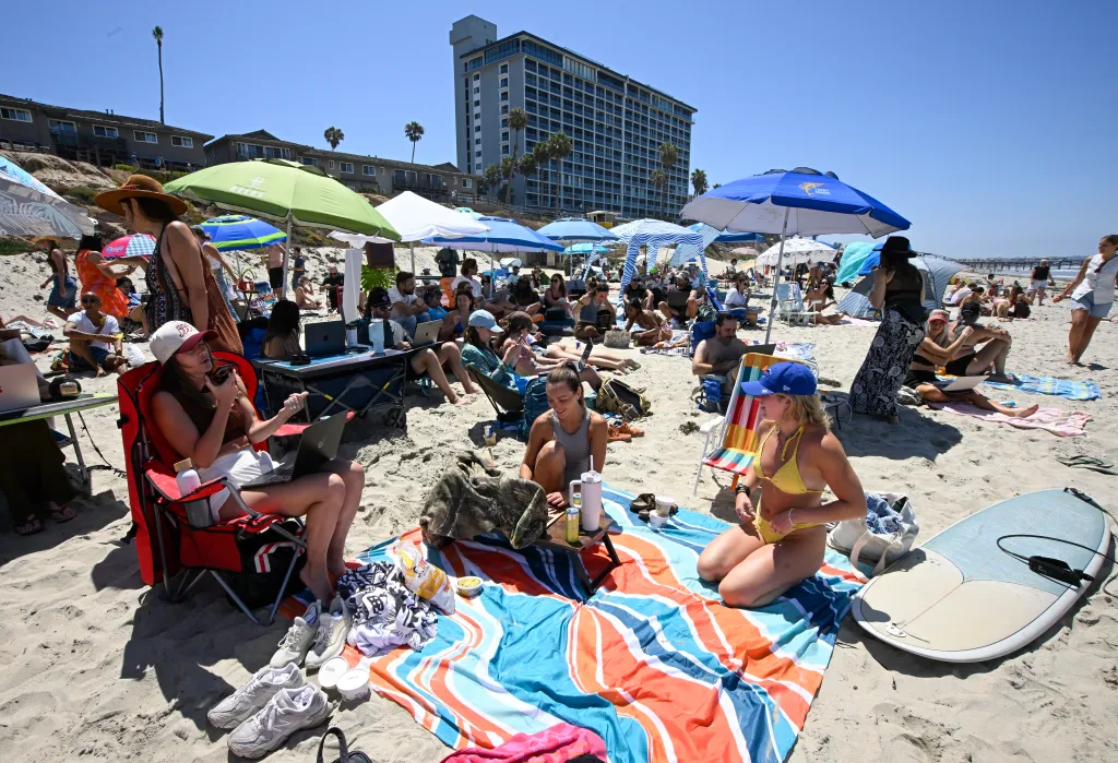 People working on laptops at a Remote Work event on a beach in San Diego.