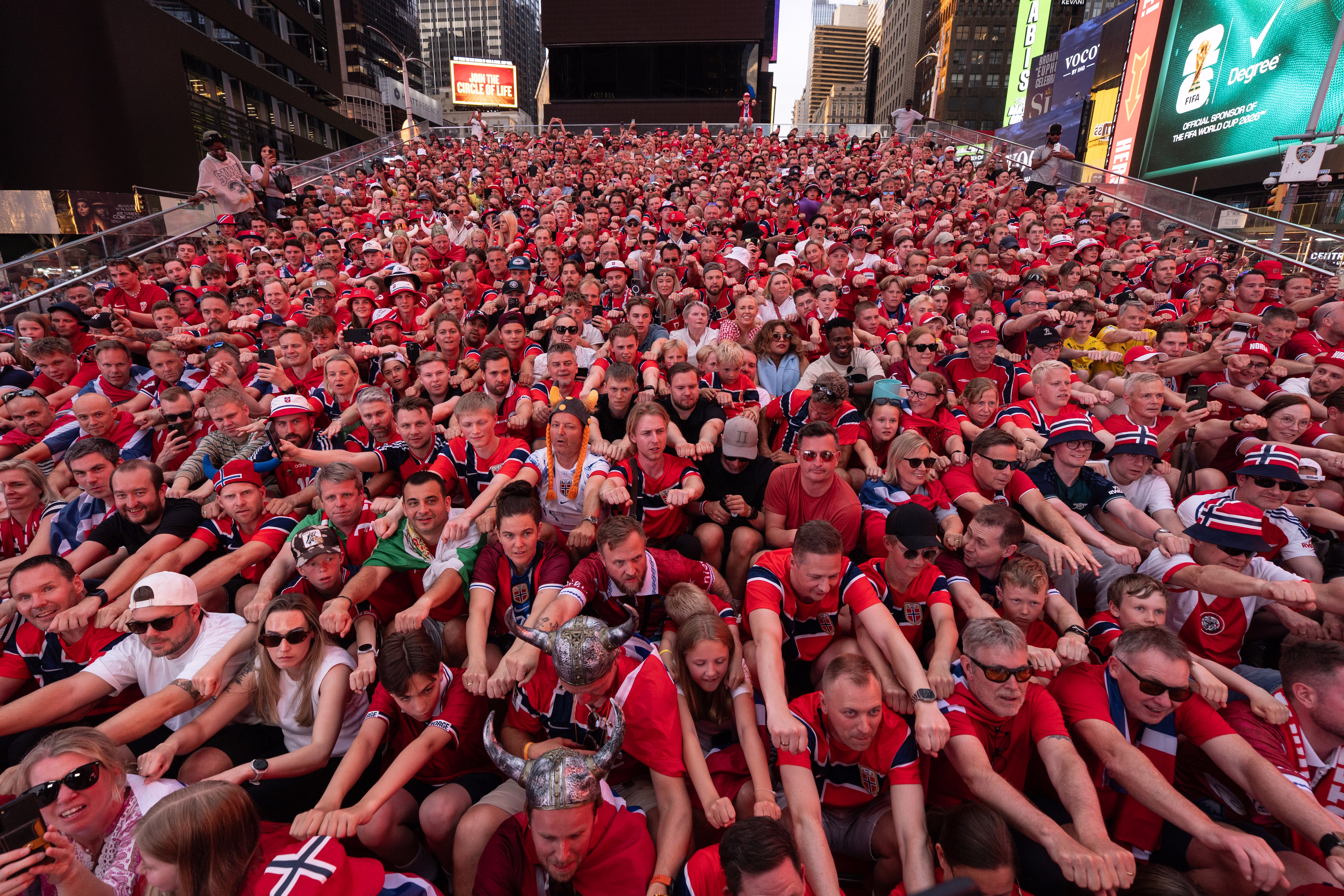 Norwegian national football team supporters, sitting in rows on an open staircase in Times Square, 'row' together in unison, cheering their team.