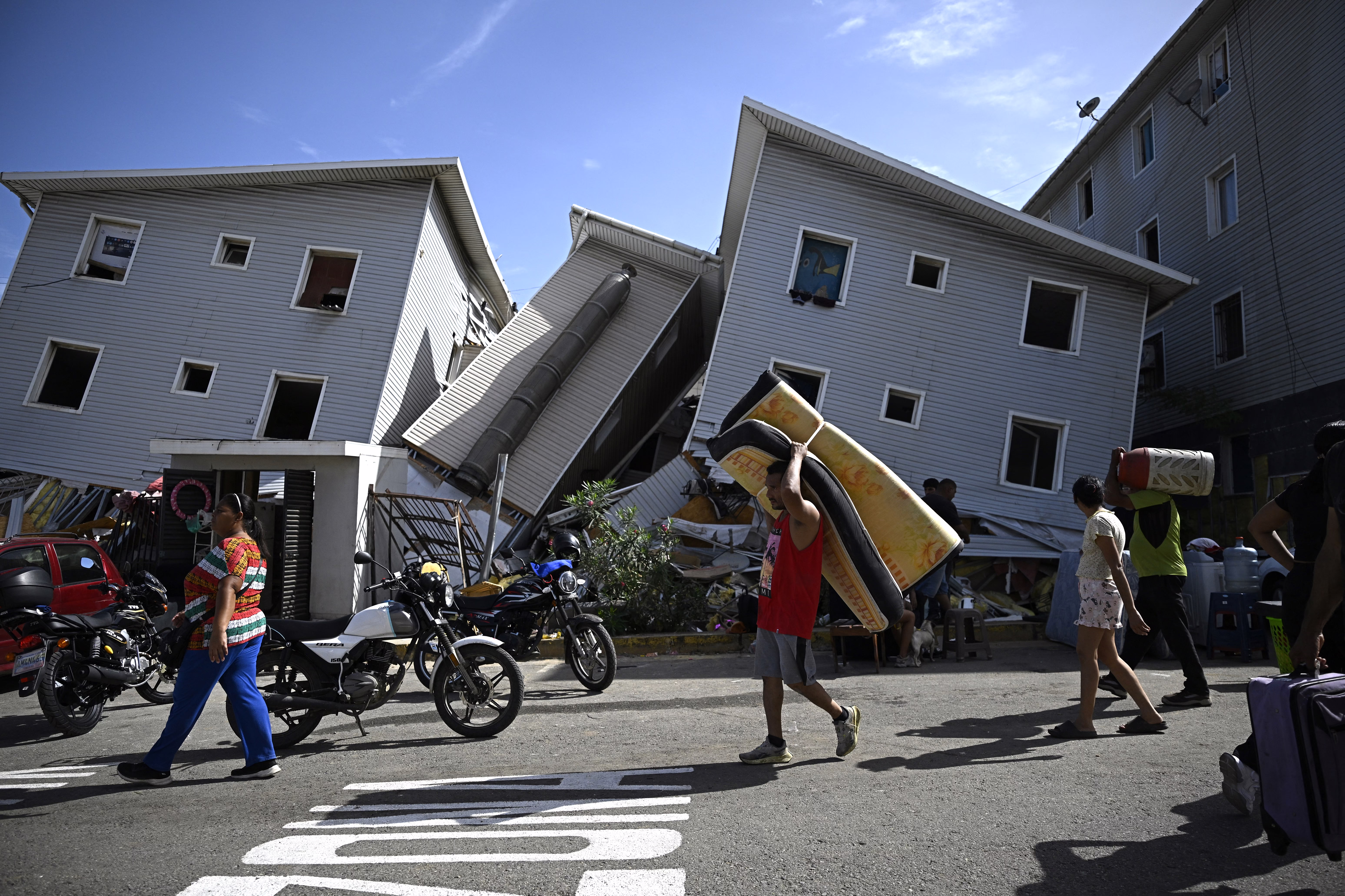 A man carries a mattress past damaged residential buildings following an earthquake.