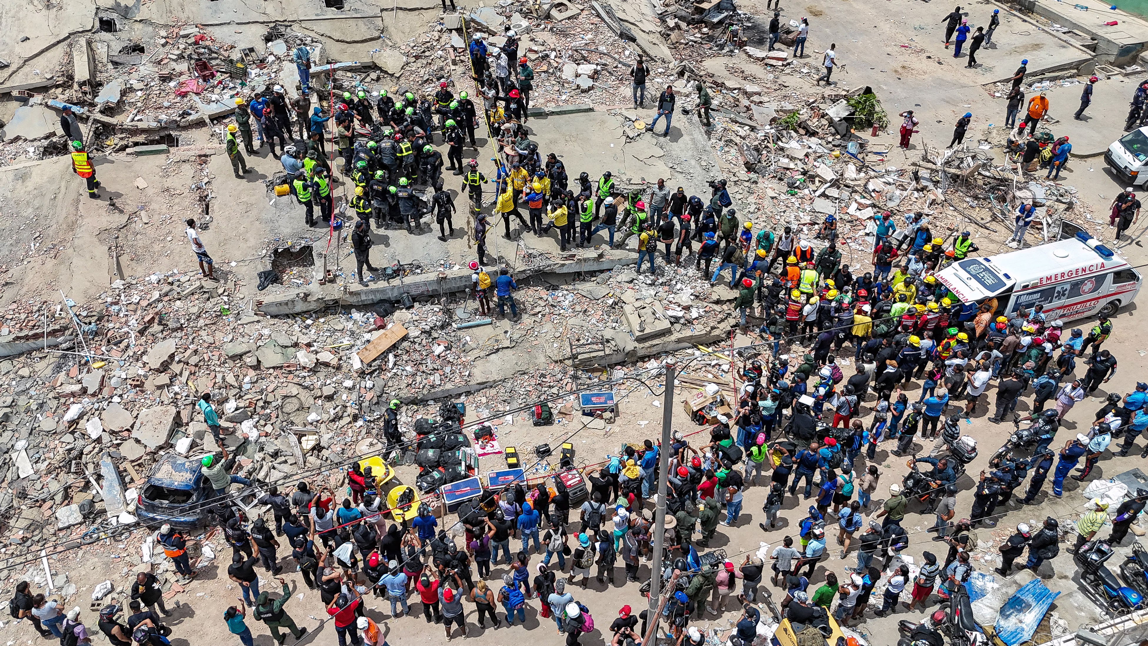 An elevated view of dozens of rescue workers on top of the rubble of a collapsed building