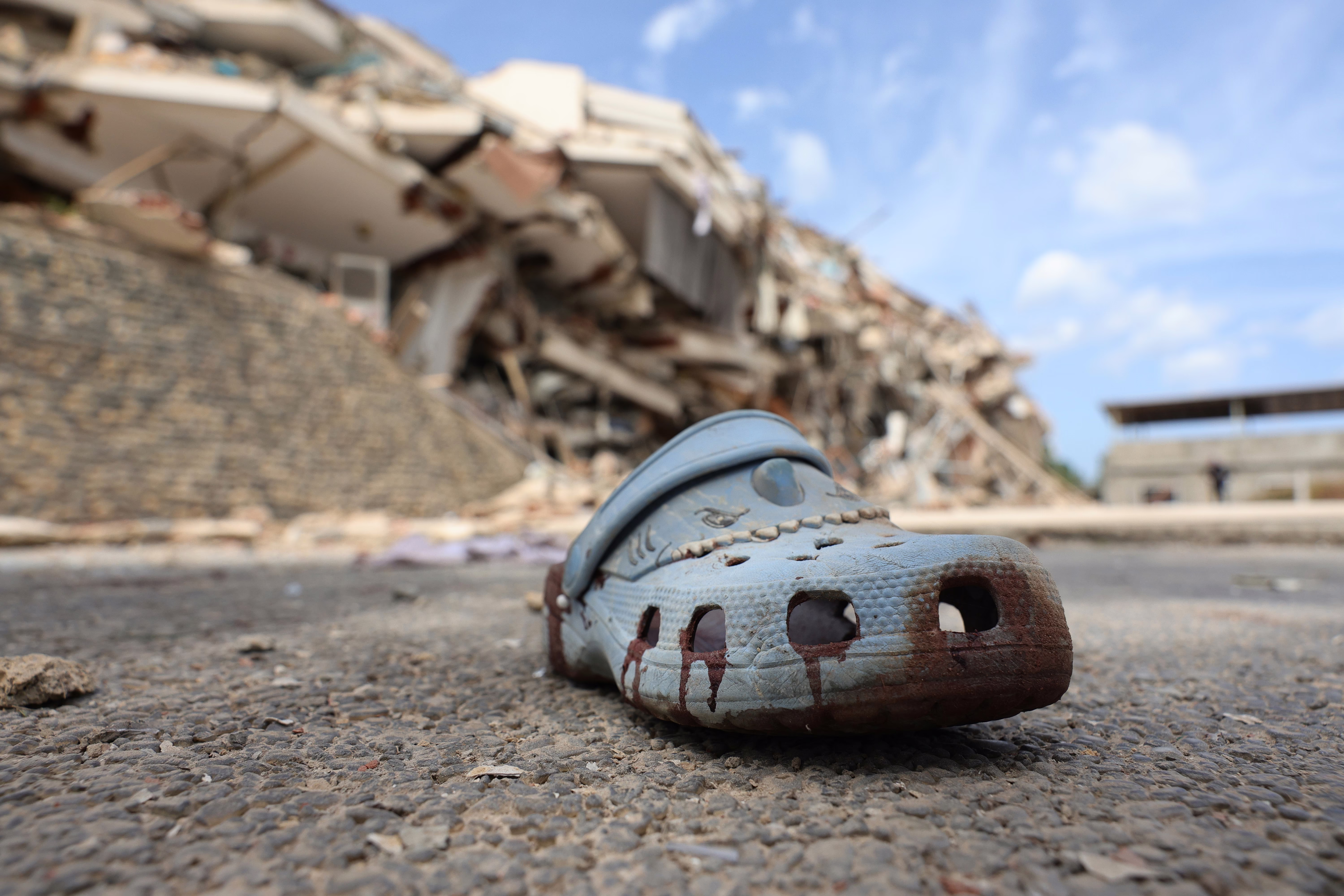 A bloodied sandal lies in the street amid debris of collapsed buildings.