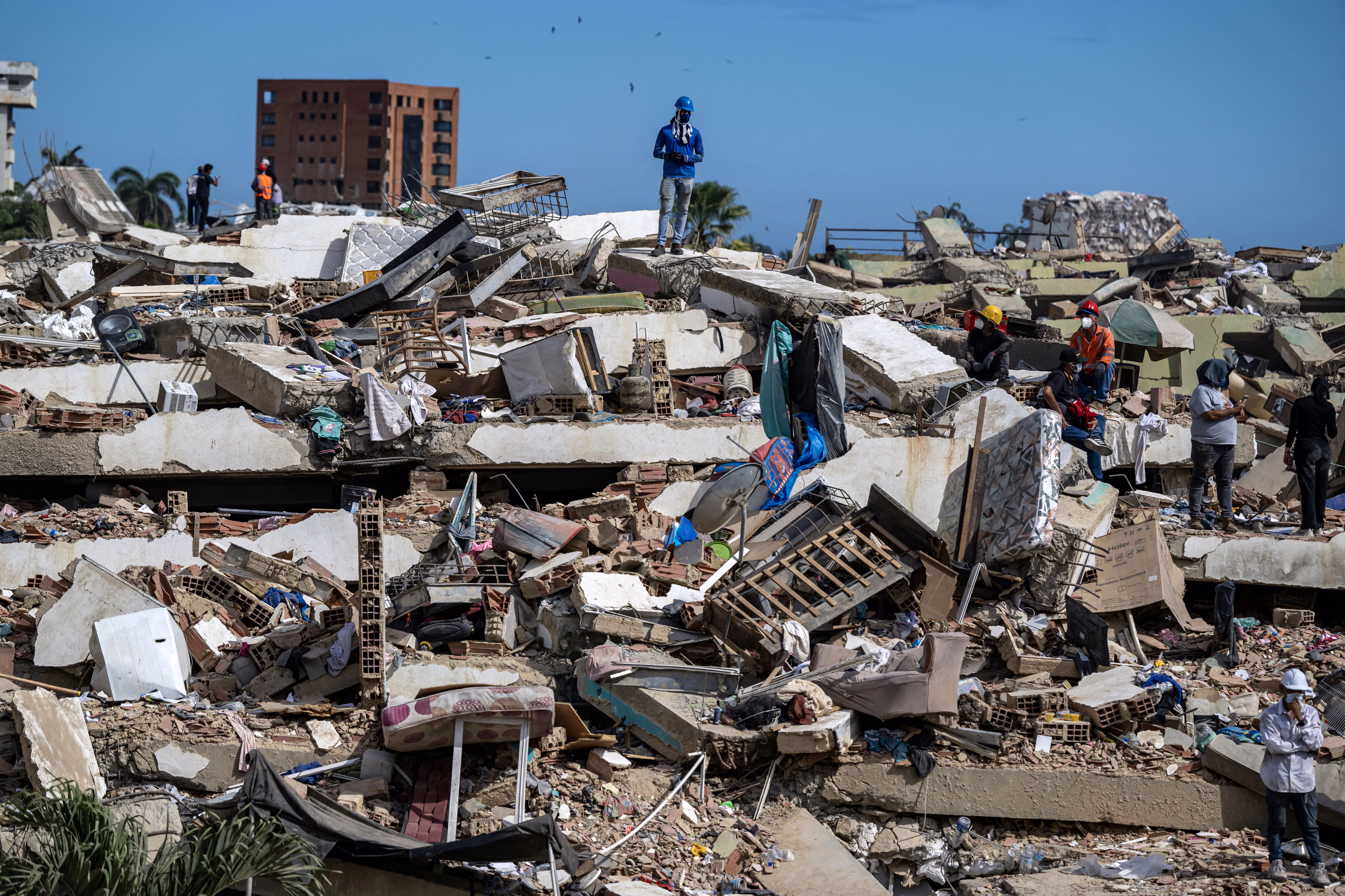 People search for survivors, walking on top of the rubble of collapsed buildings.
