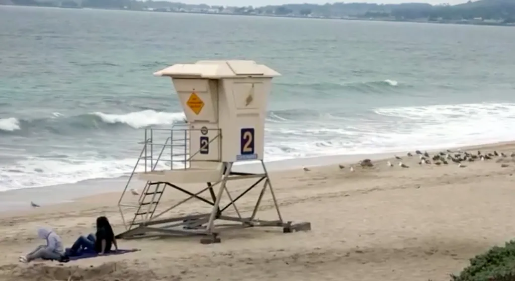 Lifeguard tower on a beach with people and the ocean in the background.