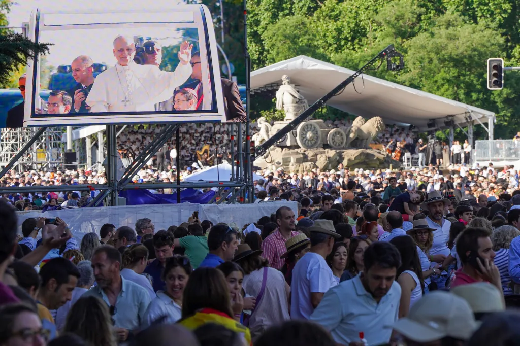 Thousands of people gather in Madrid to watch Pope Leo XIV on a large outdoor screen, with a stage and green trees in the background.