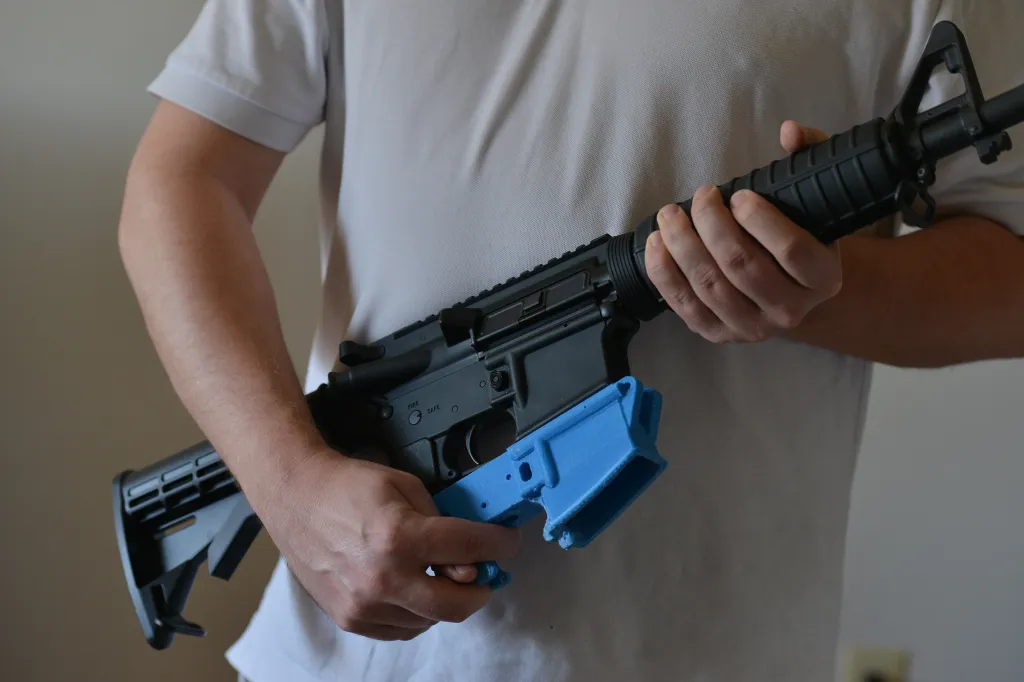 Travis Lerol holds an AR-15 assault rifle along with a rifle's lower receiver made of ABS (Acrylonitrile Butadiene Styrene) plastic that was constructed by his 3D printer at his home on Feb. 12, 2012.