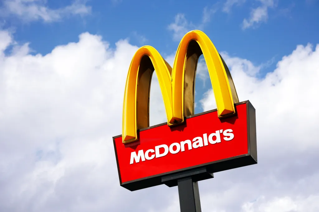 The golden arches of the McDonald's logo on a red sign against a blue sky with white clouds.