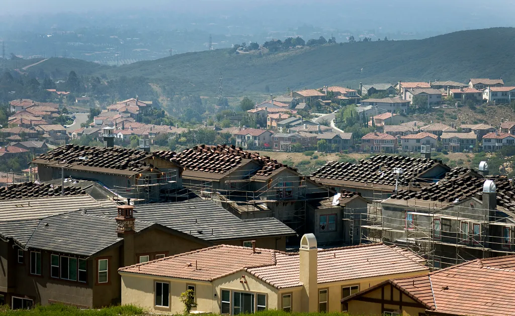 Houses under construction and completed houses dot a hilly landscape.