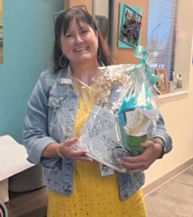 A woman smiling while holding a gift basket.