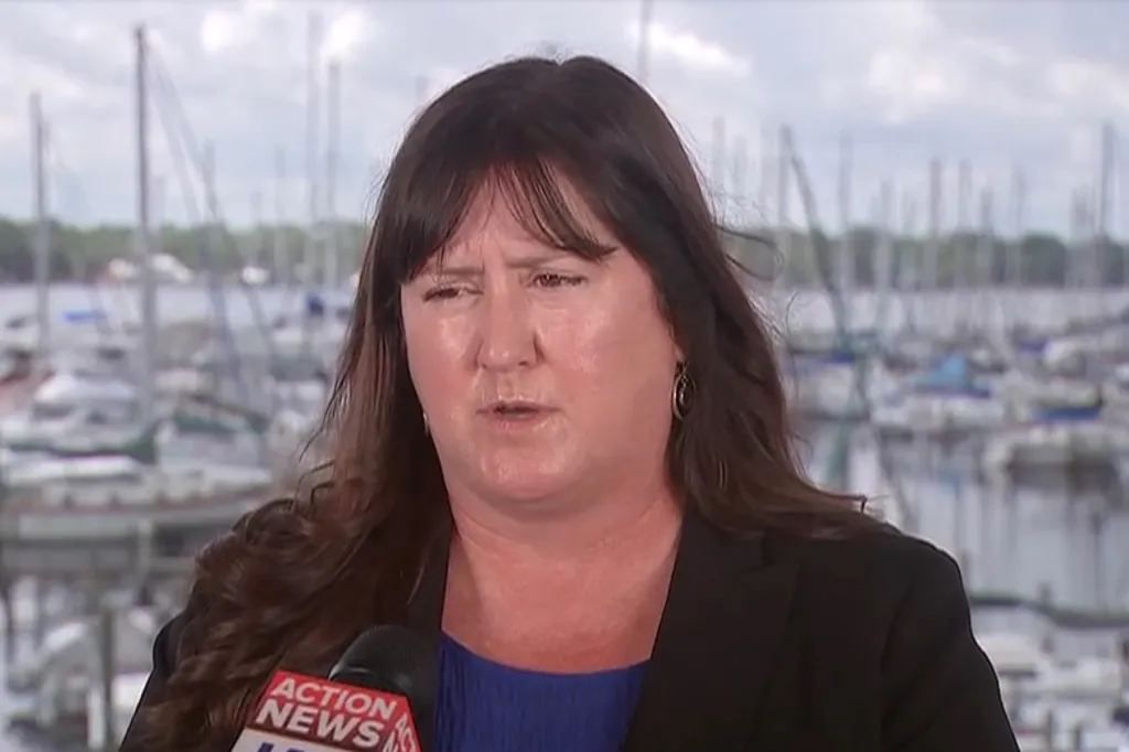 Katie O’Connell, principal of Trout Creek Academy, being interviewed with a body of water and boats behind her.